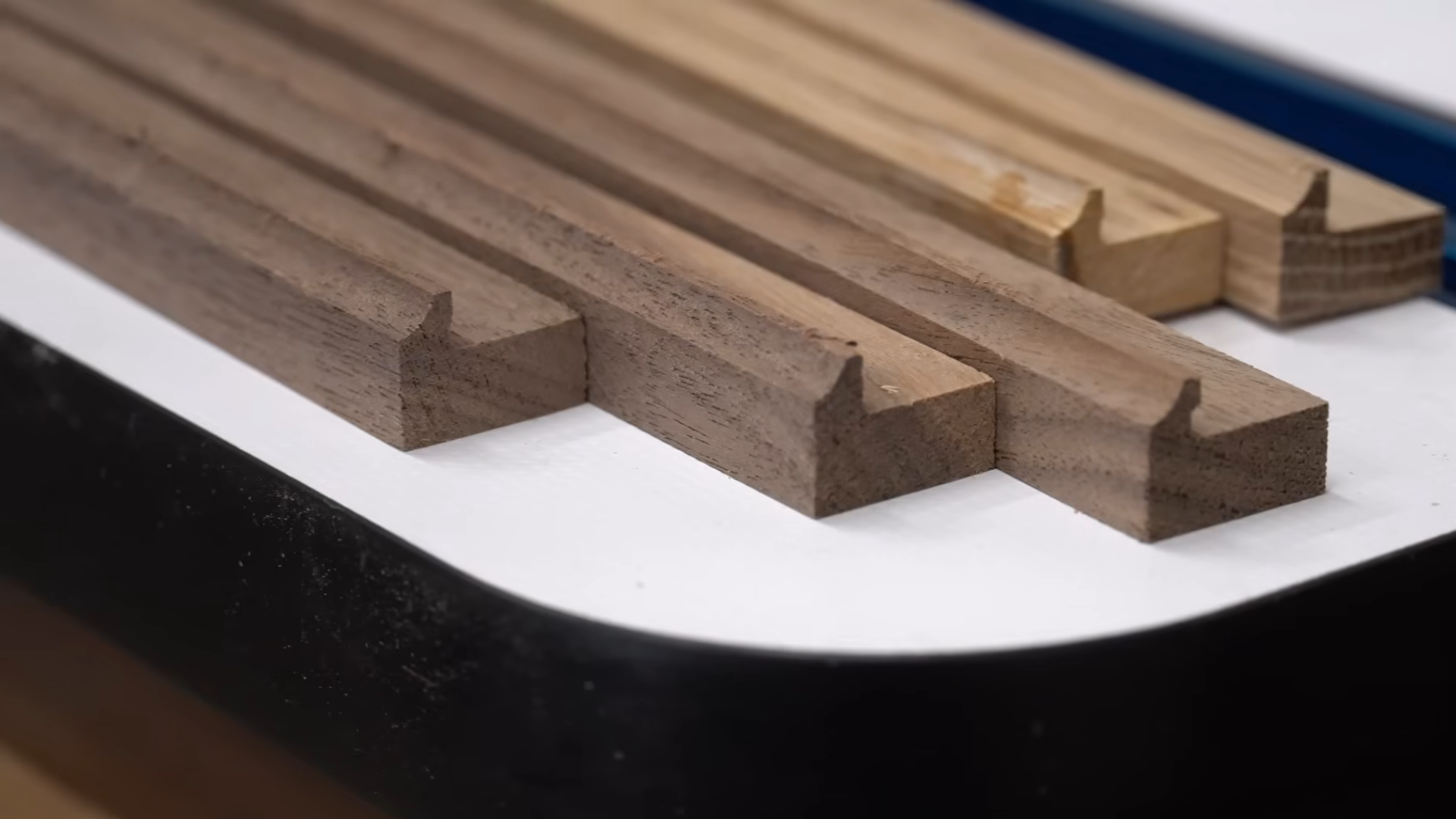 close view of grooved wooden strips with precision cut profiles arranged on a white tabletop in a woodworking shop