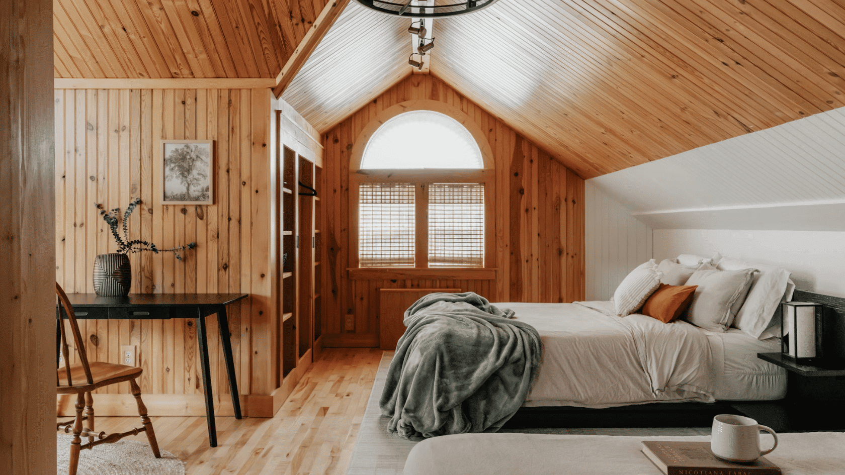 Cozy attic bedroom with wood paneled vaulted ceiling ceiling fan and large arched window