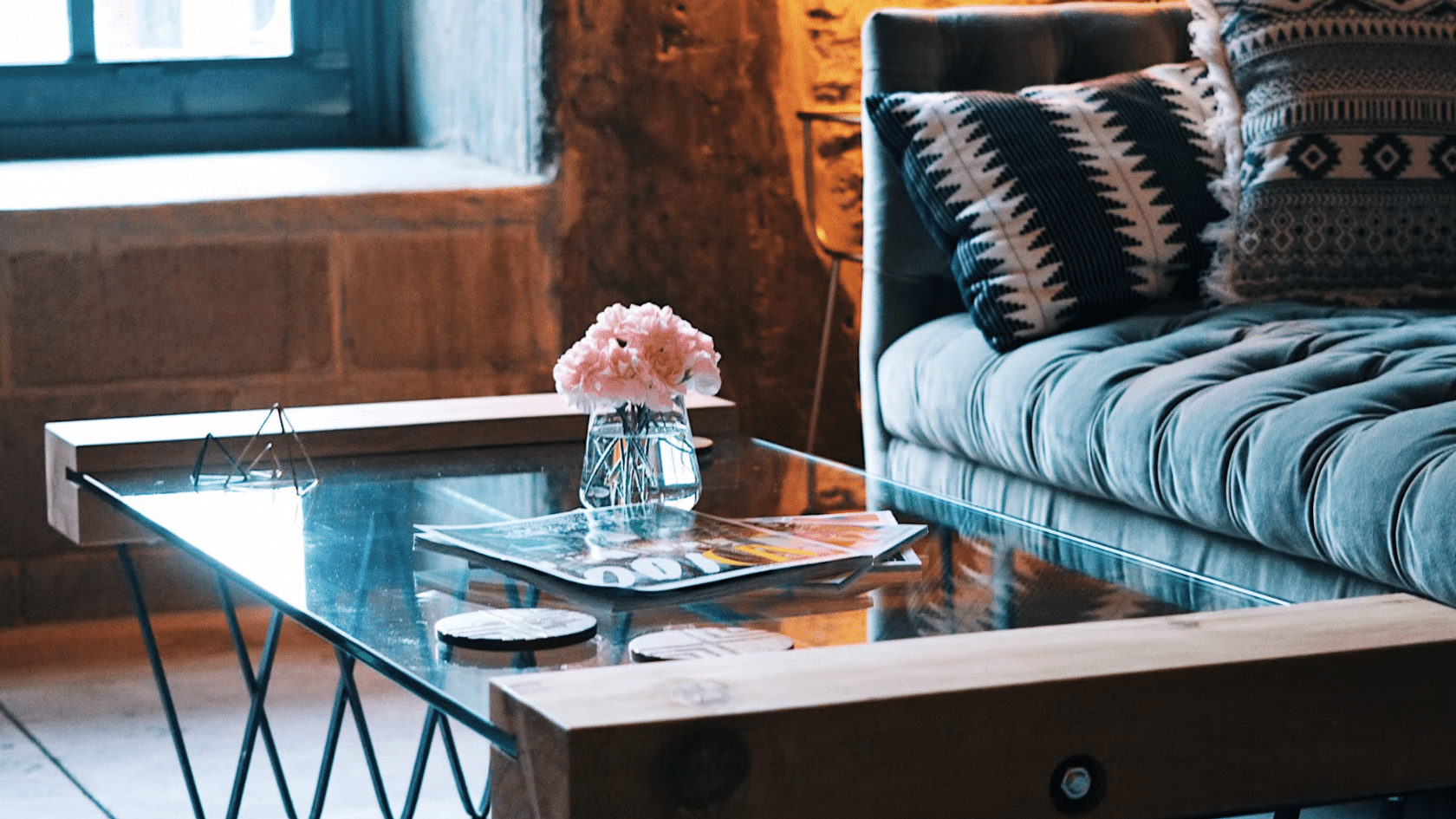 cozy living room corner with tufted sofa patterned cushions and a glass coffee table holding flowers and magazines