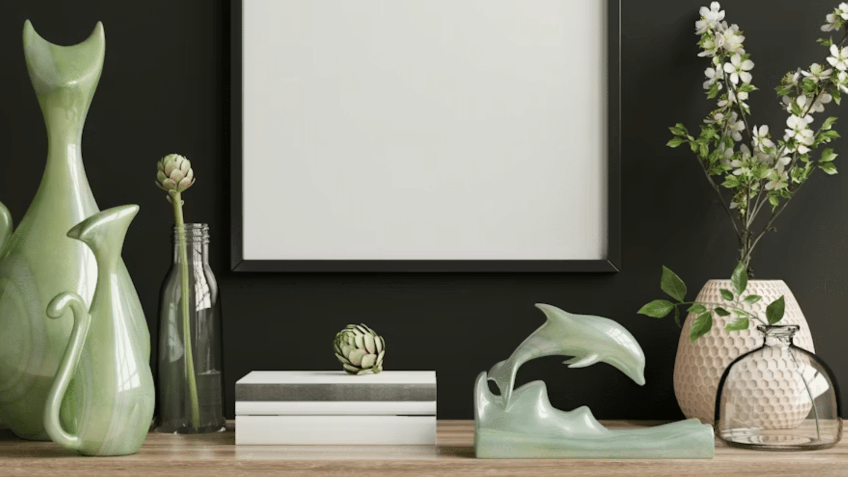 decorative tabletop display with ceramic vases glass bottles flowers and a blank framed print against a dark wall