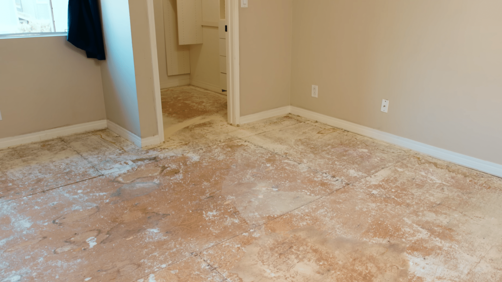 empty room with exposed plywood subfloor showing adhesive residue and wear marks prepared for new flooring installation