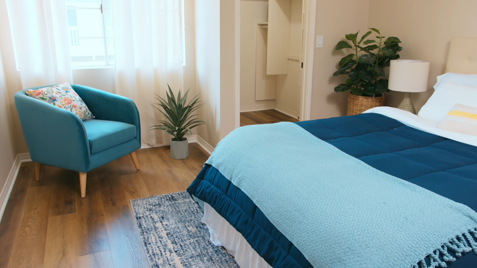 finished bedroom featuring wood look vinyl plank flooring with a blue bed armchair plants and natural light from large windows