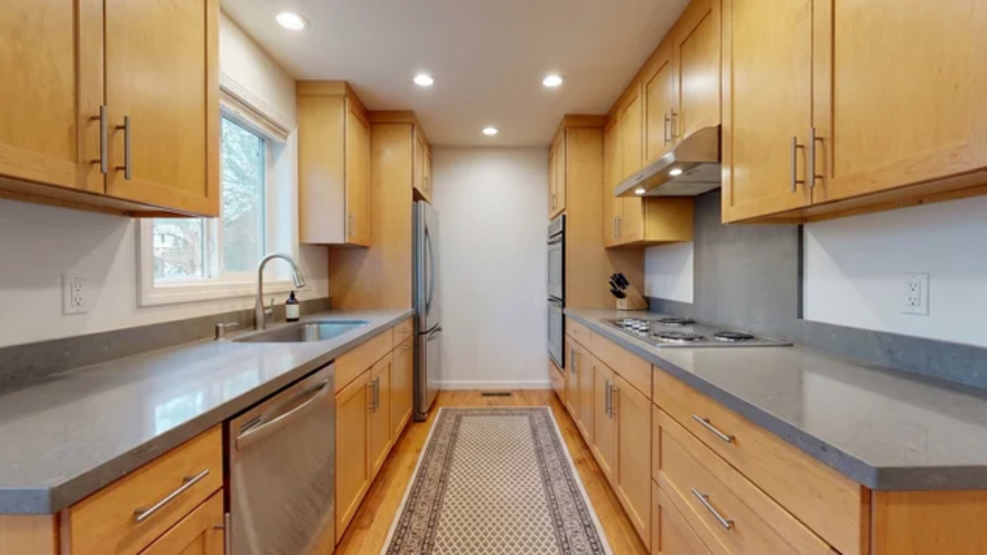 Narrow kitchen with two parallel cabinet walls, countertops, sink, stove, and refrigerator on opposite sides