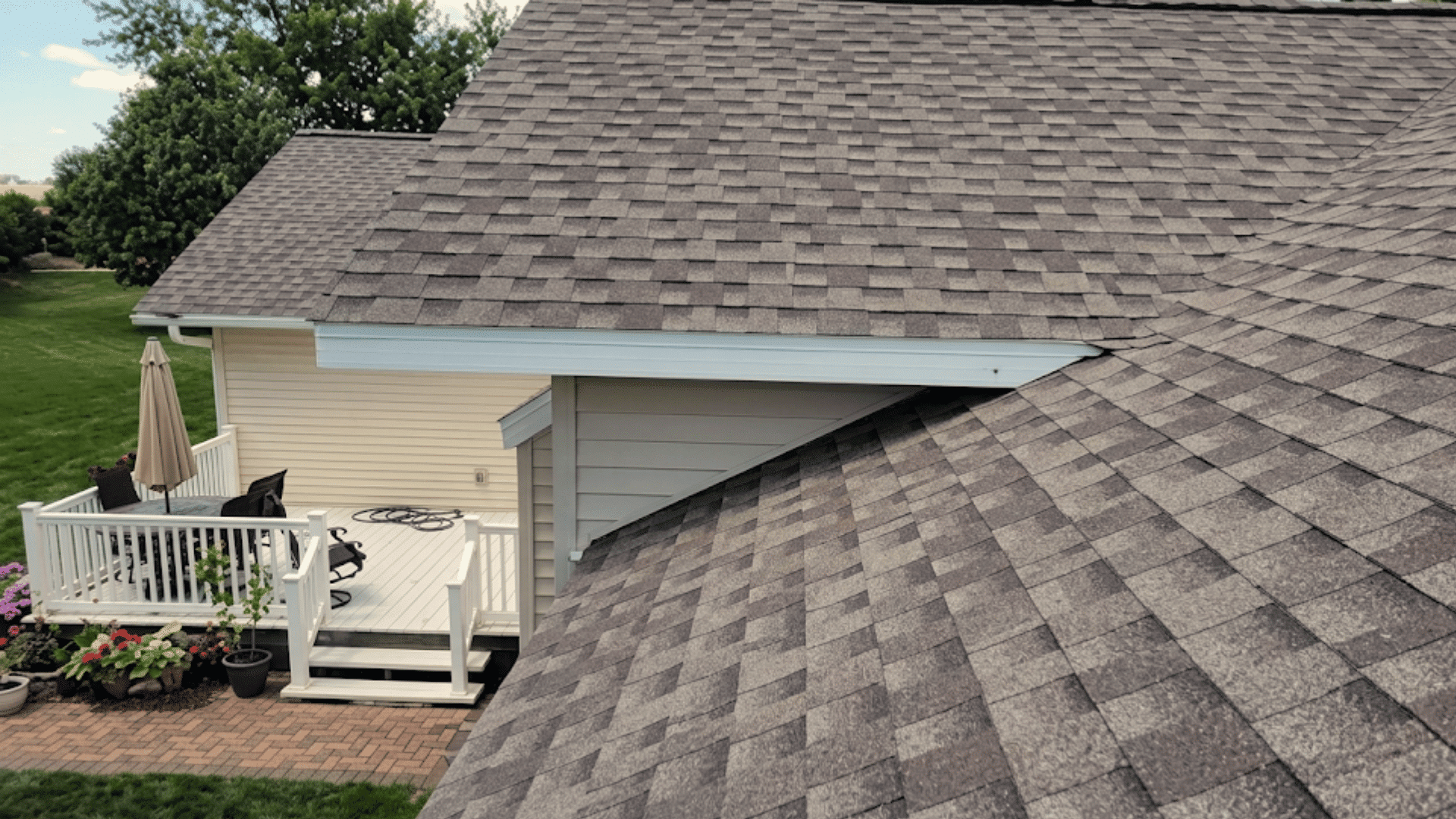 gray asphalt shingle roof covering a modern home with a white deck and landscaped backyard view