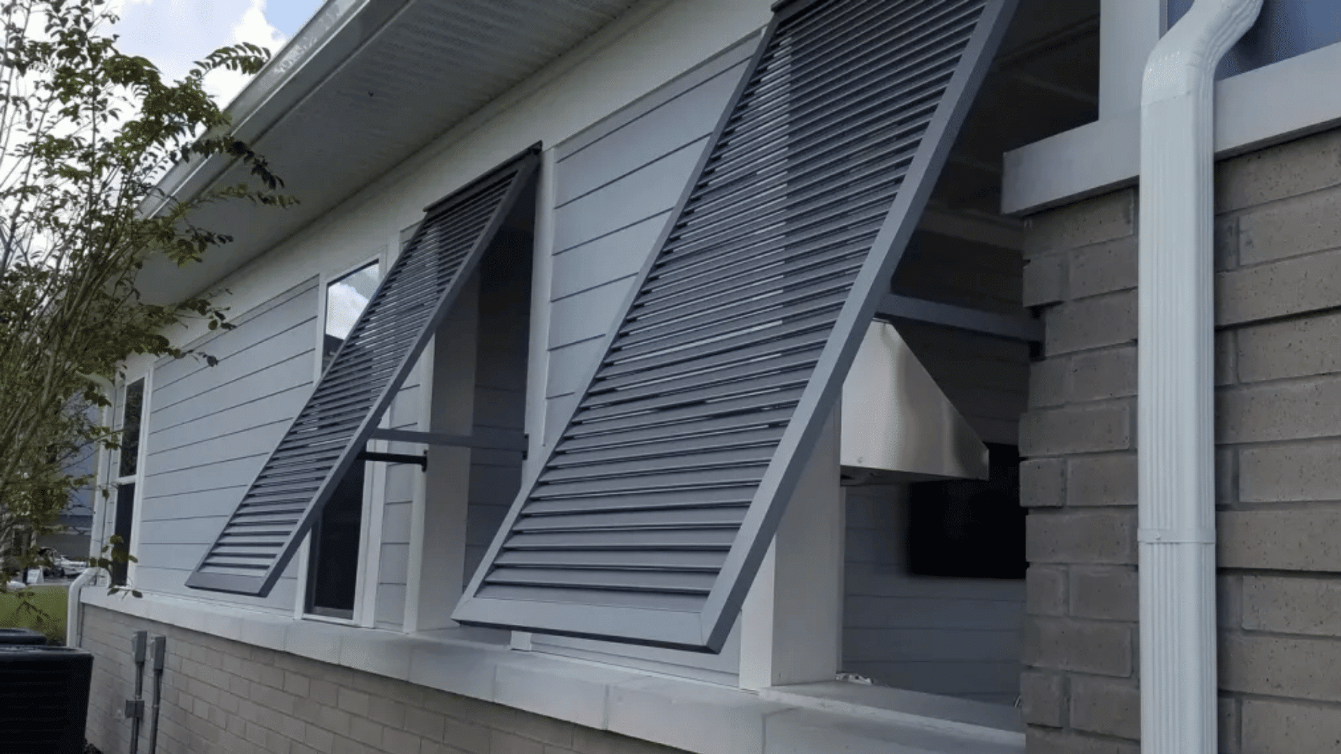 gray bahama shutters mounted above windows on a modern home exterior providing shade airflow and weather protection
