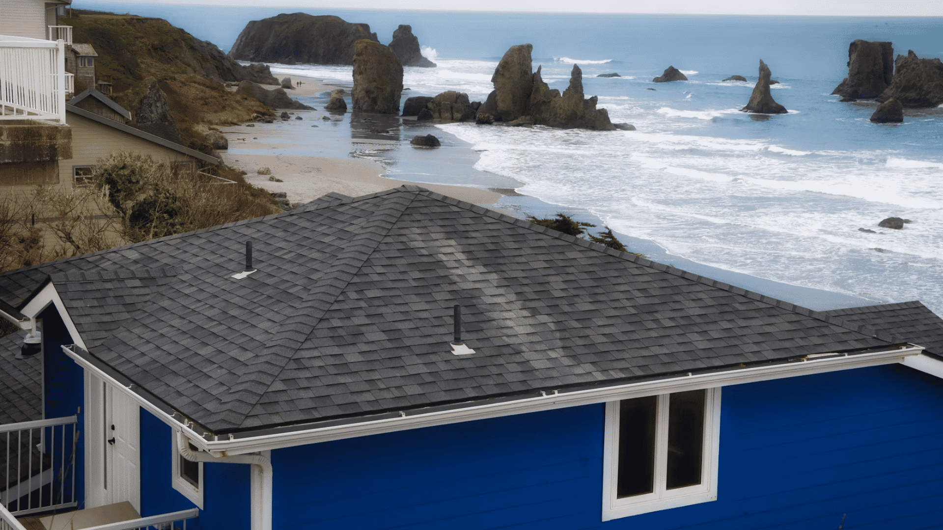 gray shingle roof of a blue coastal house overlooking rocky shoreline and ocean waves