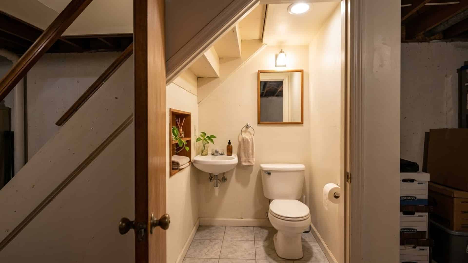 half bath under stairs in basement with compact toilet and sink light colors and smart space saving layout