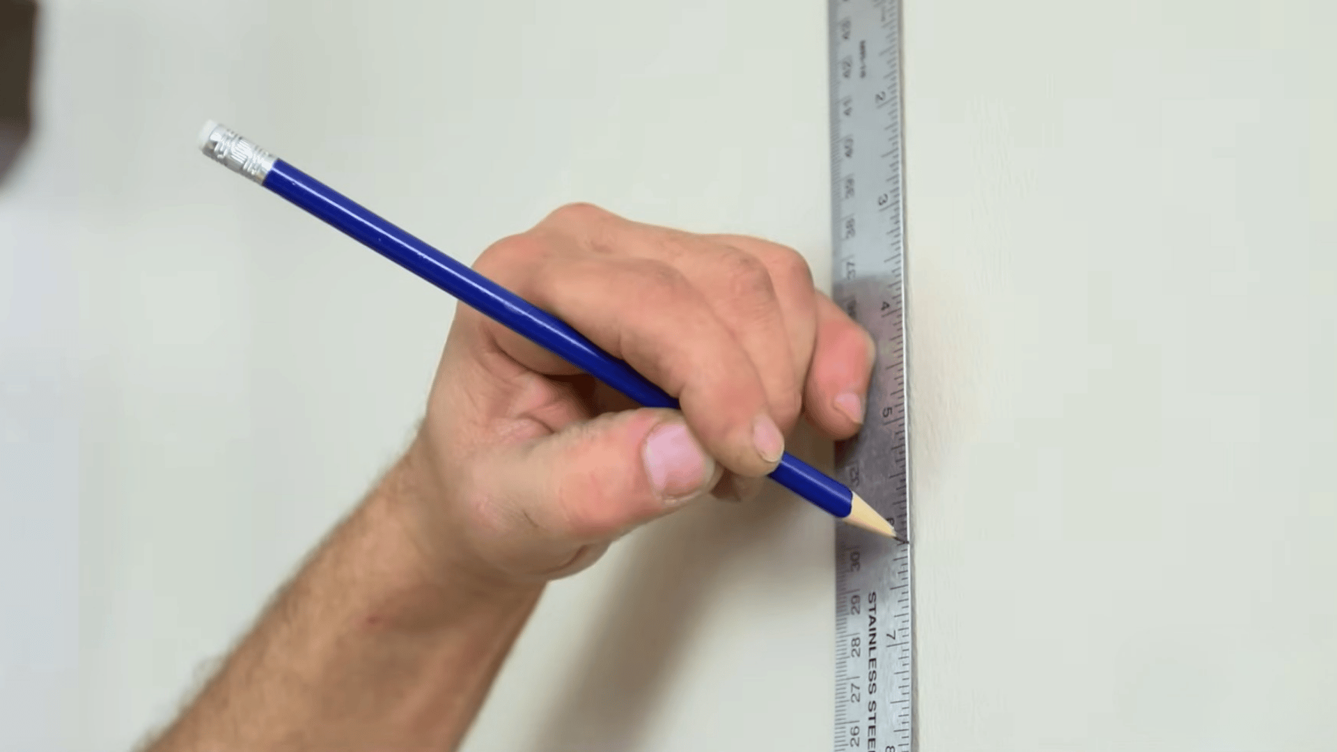hand holding a pencil against a ruler to mark an exact measurement on a wall for picture hanging hardware placement