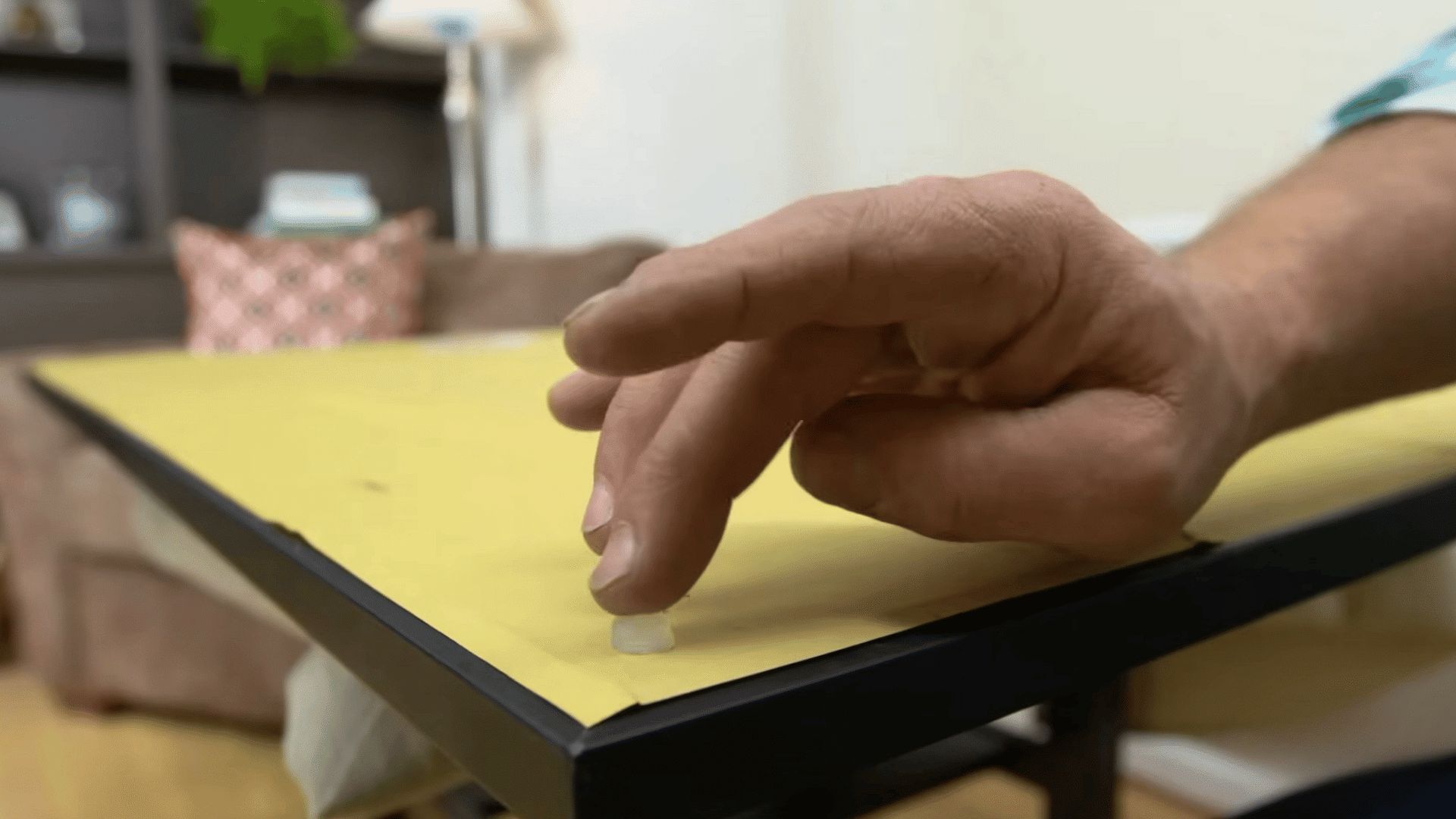 hand placing a small rubber bumper on the back corner of a framed picture to protect the wall and keep it level when hung