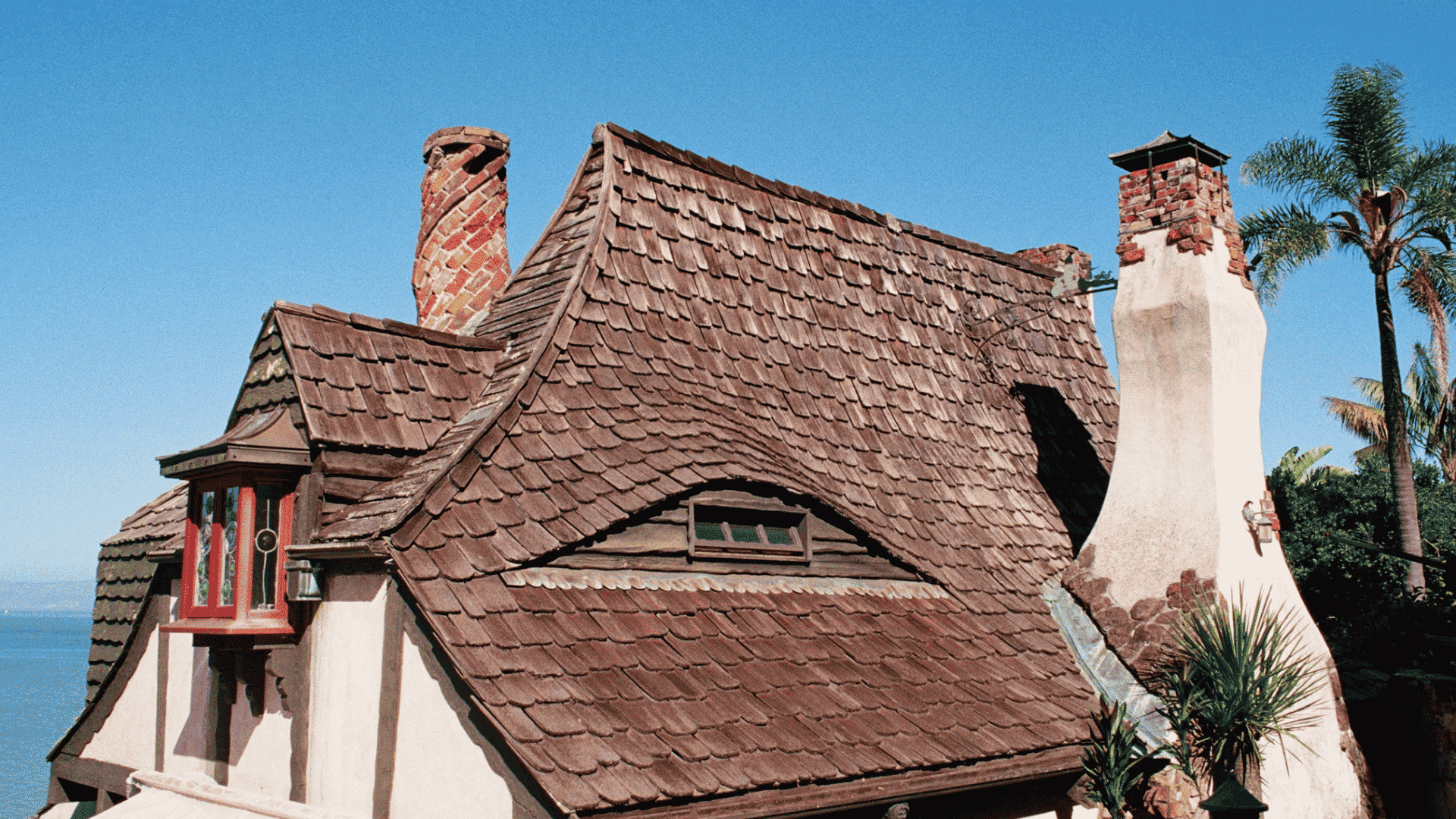 historic house with curved wood shingle roof brick chimneys and palm trees beneath a clear blue sky