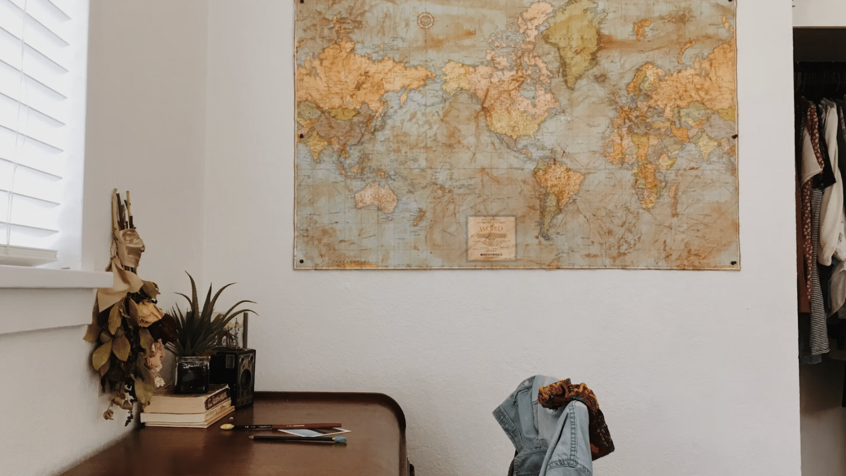 home workspace with a vintage wooden desk world map wall art small plant and chair beside an open closet area