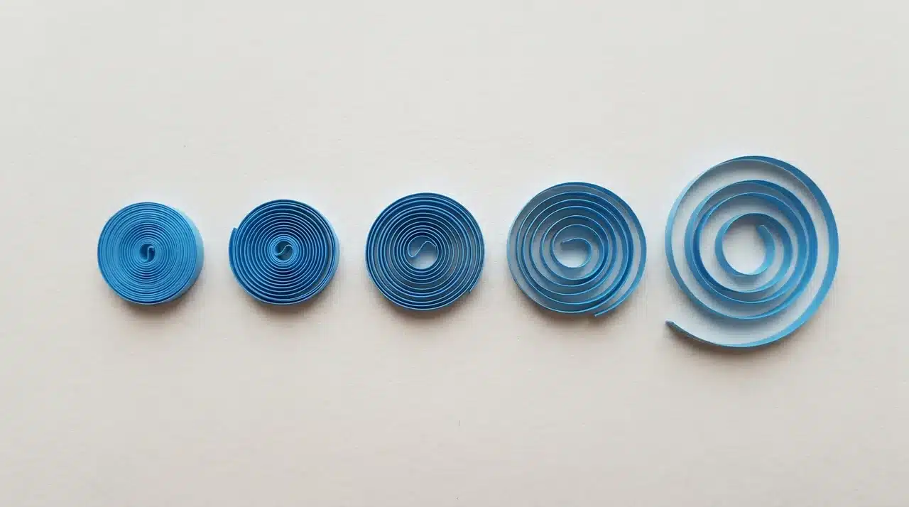 Row of paper quilling coils ranging from tight compact rolls to loose open coils on a flat surface
