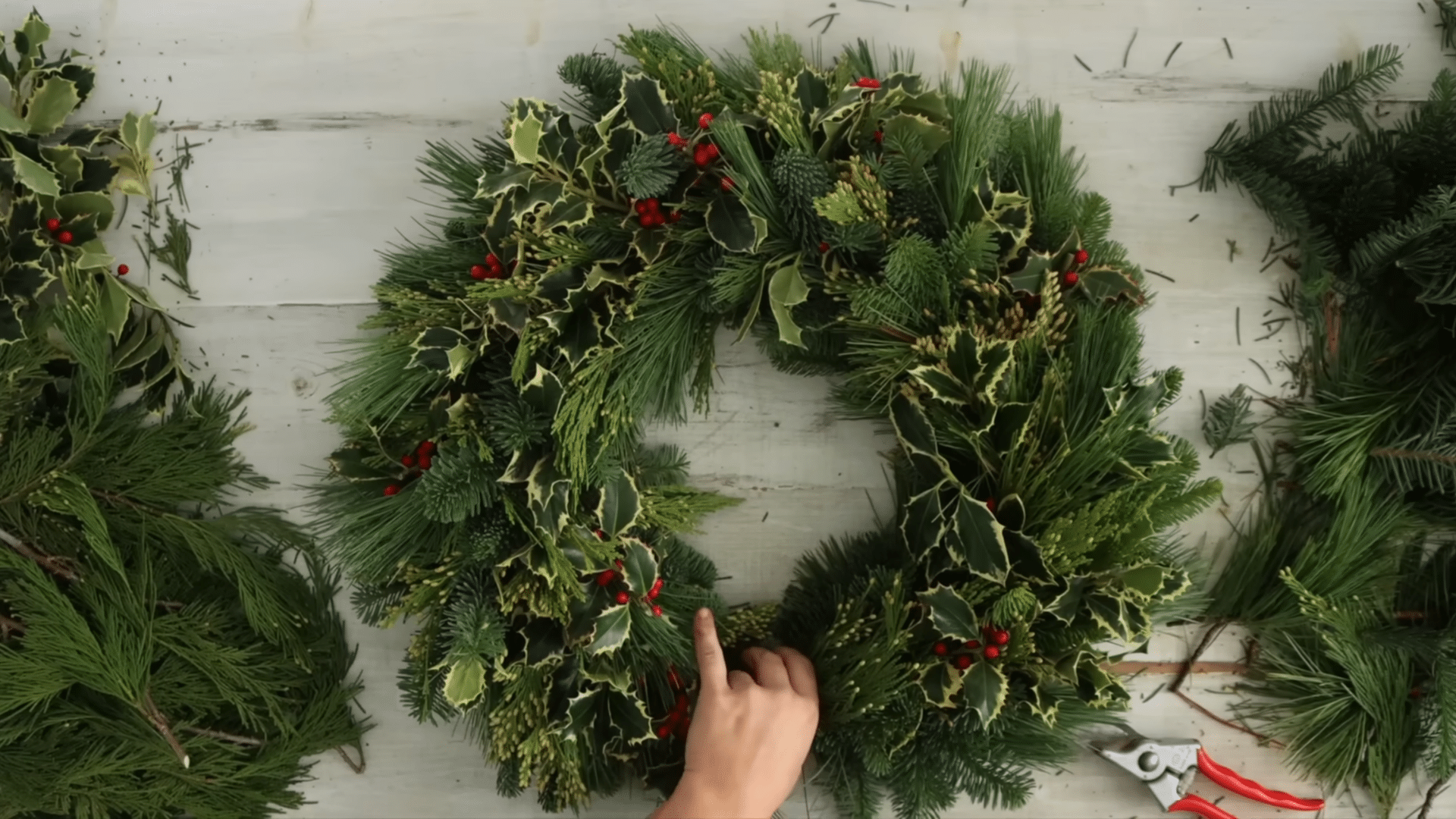 layering overlapping evergreen bundles around the frame to build a full balanced wreath