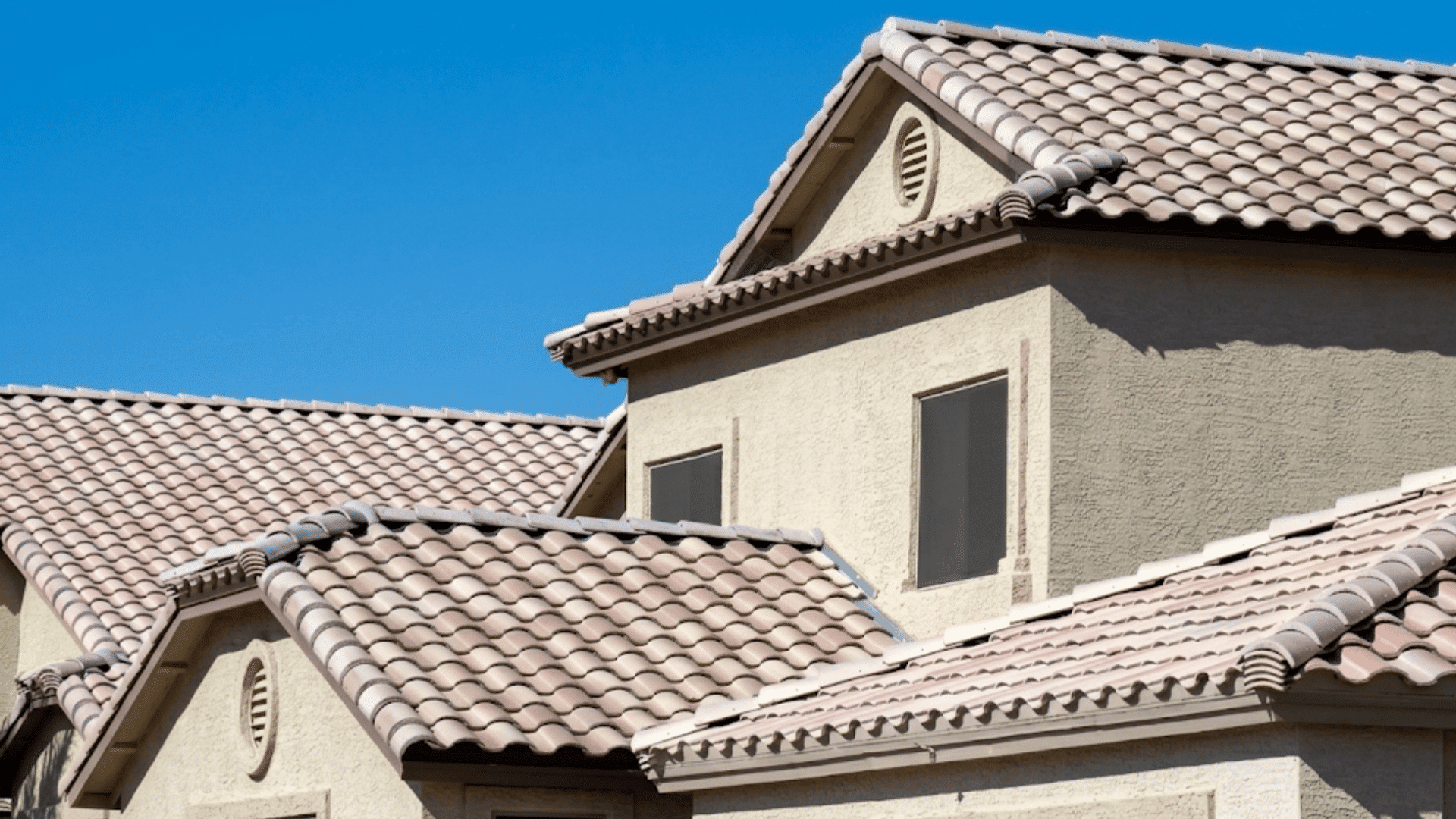 light colored clay tile roof on a multi story home with textured walls under a clear blue sky