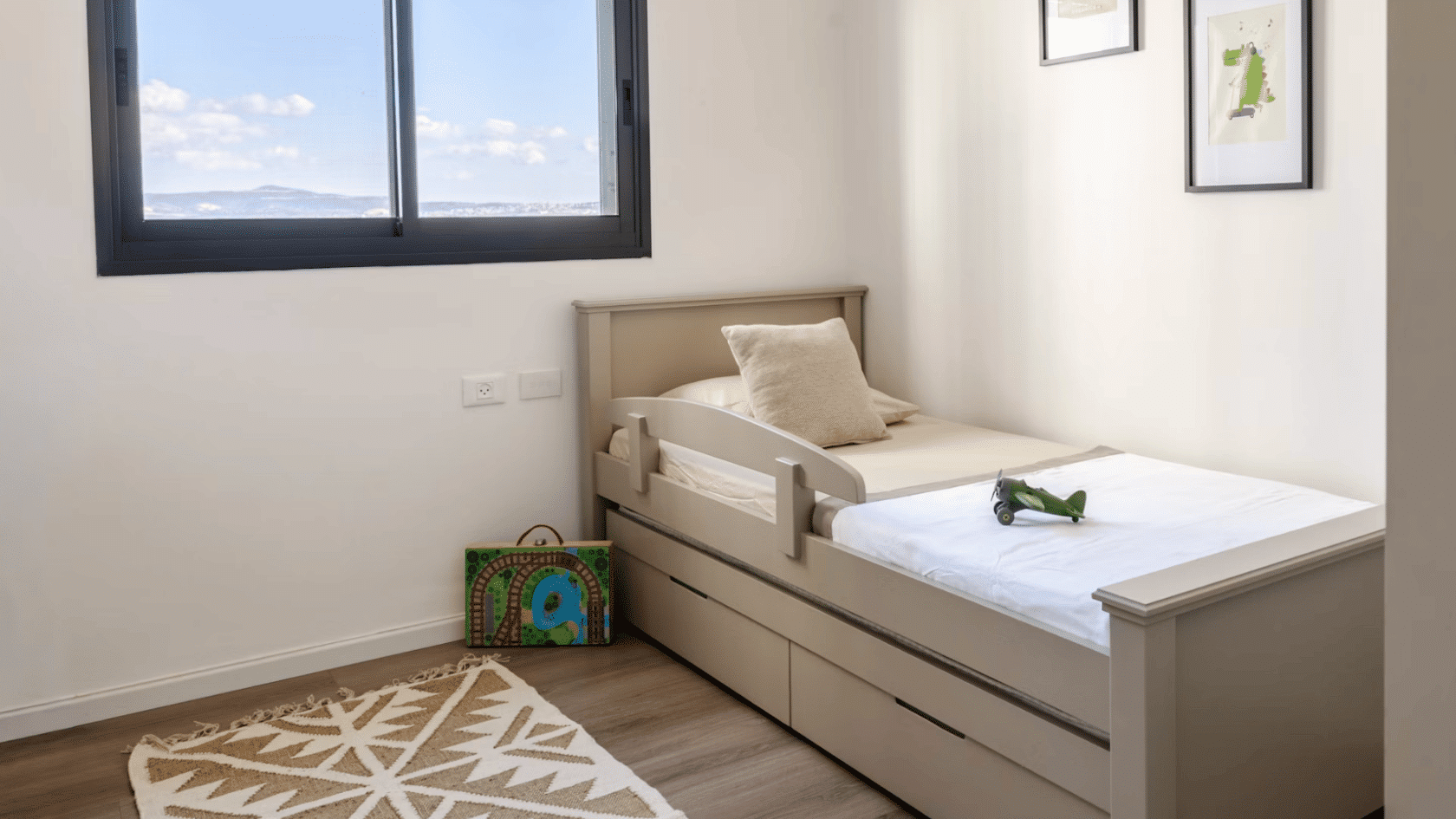 minimal childrens bedroom with a single bed framed artwork patterned rug and large window bringing in natural light