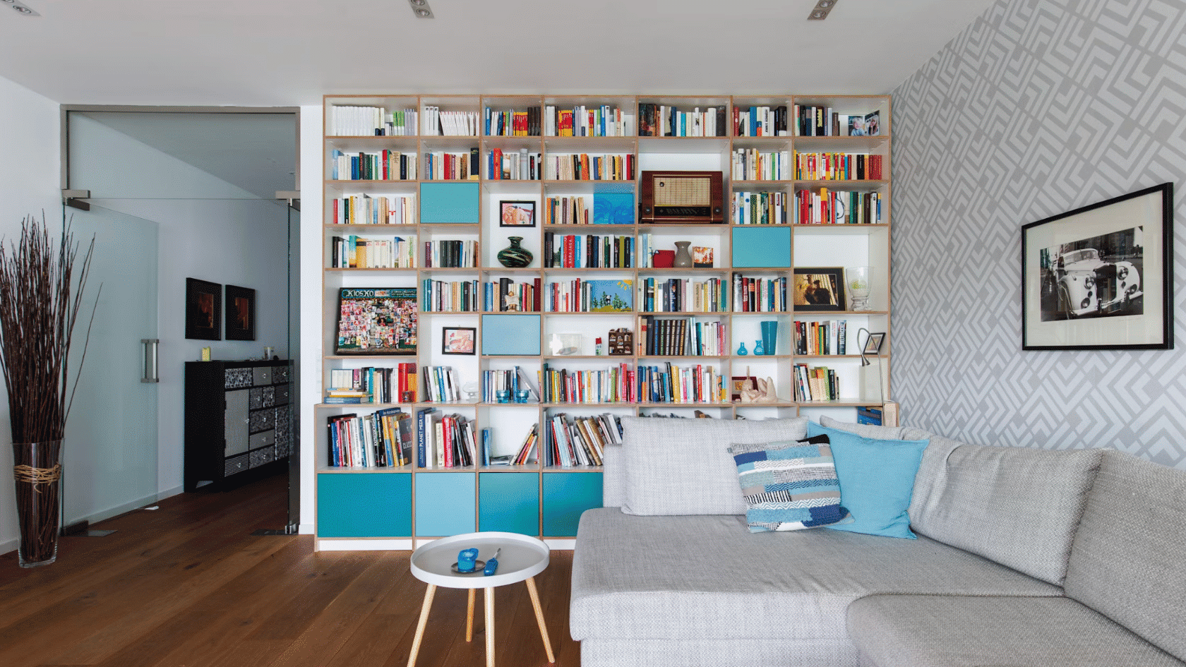 modern living room with a gray sectional sofa small round table and a wall length bookshelf filled with books and decor