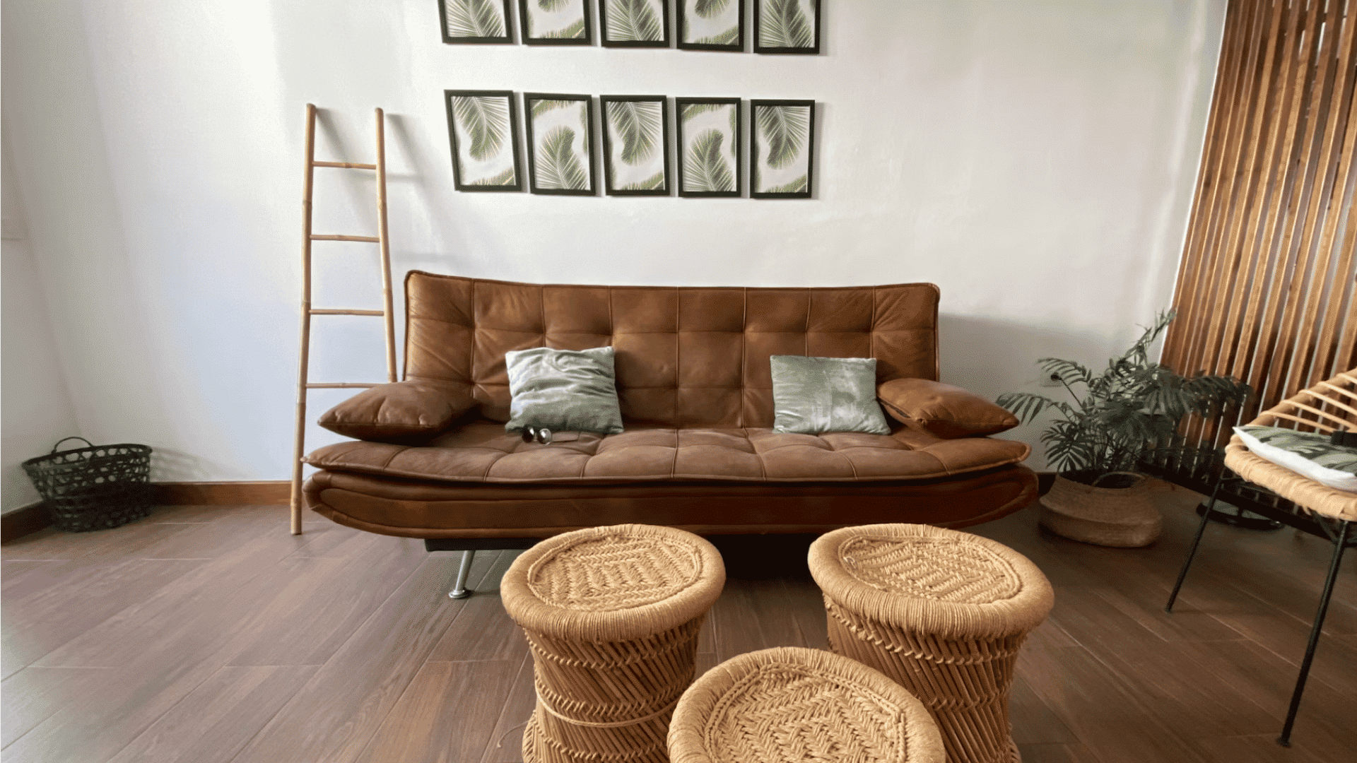 modern living room with brown leather sofa woven stools framed leaf artwork and wood flooring in bright space