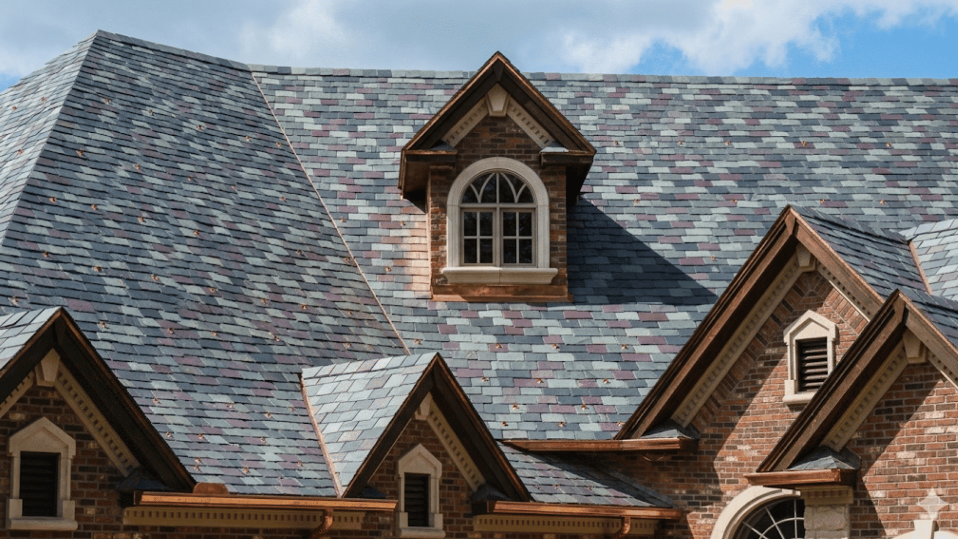 multicolored slate roof on a brick house with dormer windows and steep gable roof design under cloudy sky