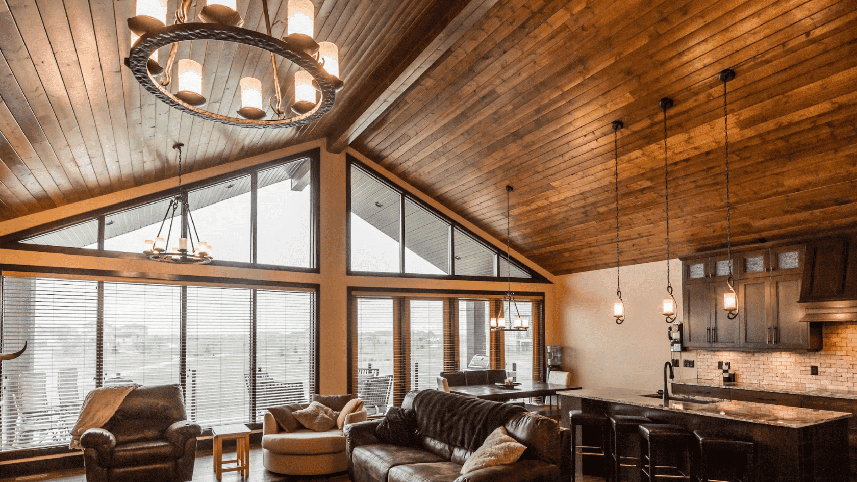 Open concept living room and kitchen with dark wood vaulted ceiling large windows and pendant lighting