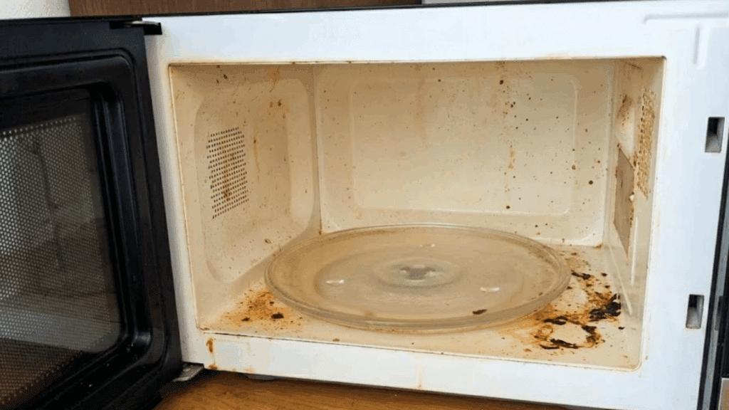 How to Clean Your Microwave: Easy Tips and Tricks open microwave with stained interior and glass turntable showing baked on food splatters and grease buildup