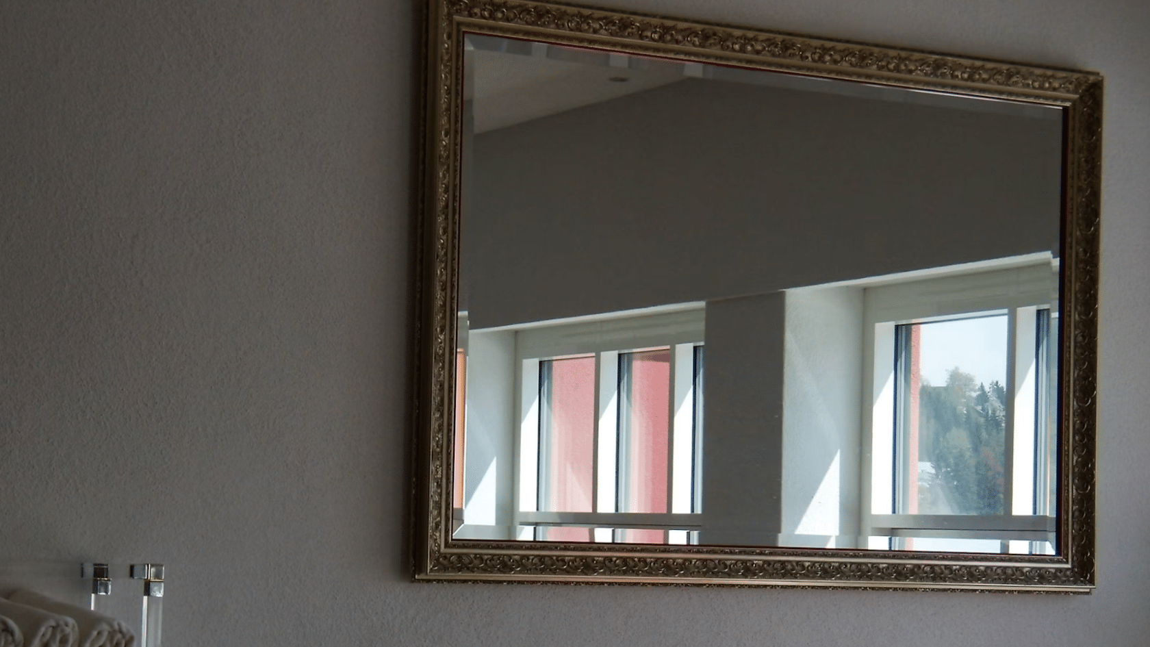 ornate framed wall mirror reflecting sunlit windows in a minimalist room with neatly stacked white towels