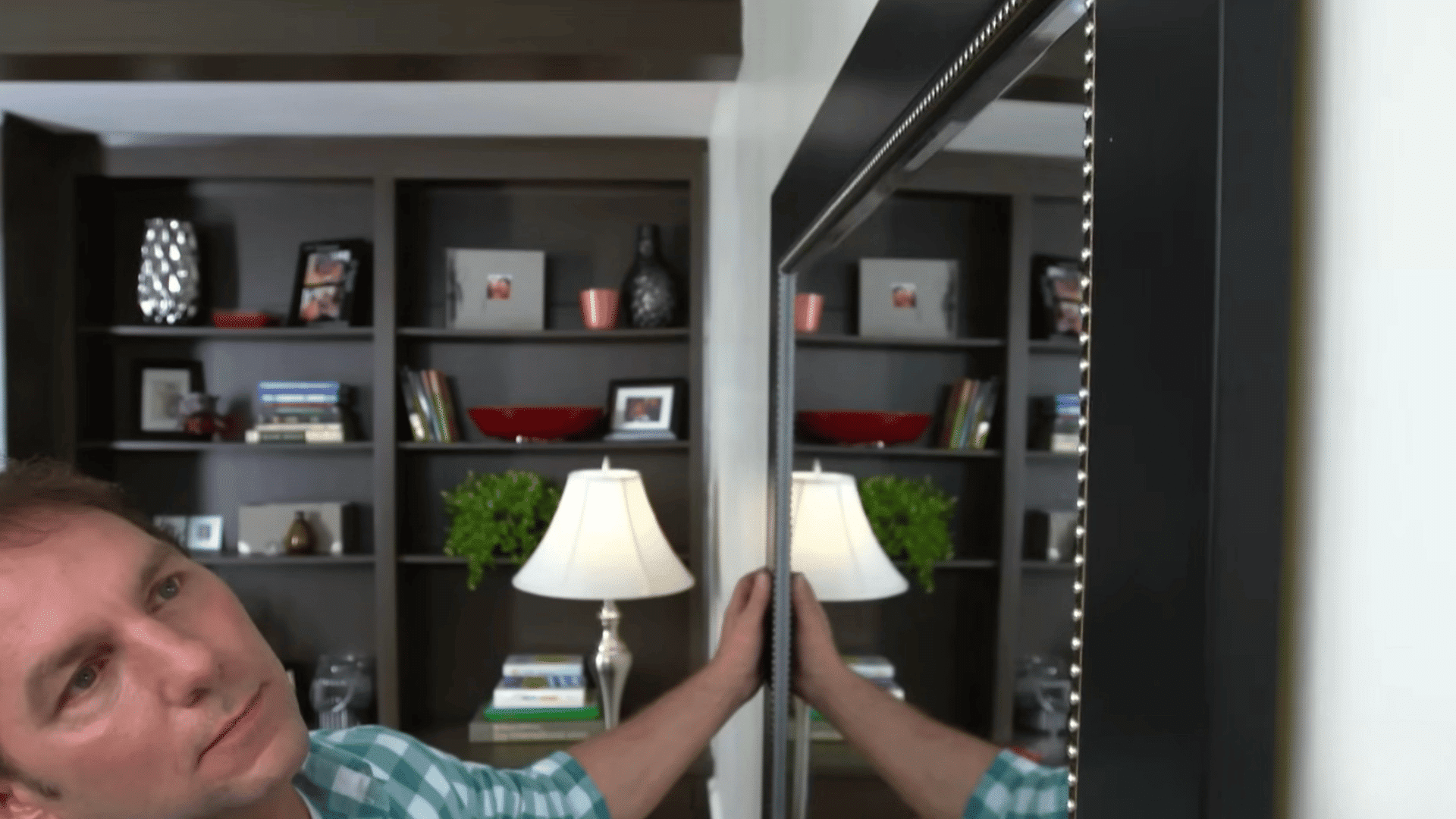 person adjusting and checking the alignment of a large framed mirror after mounting it securely on a wall in a living room setting