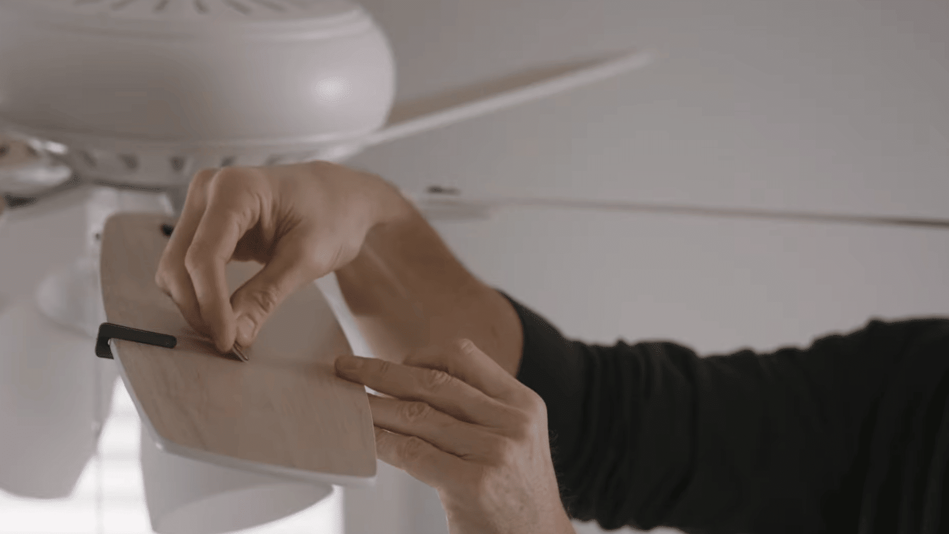 person attaching a balancing weight to a ceiling fan blade after finding the correct position to reduce wobbling