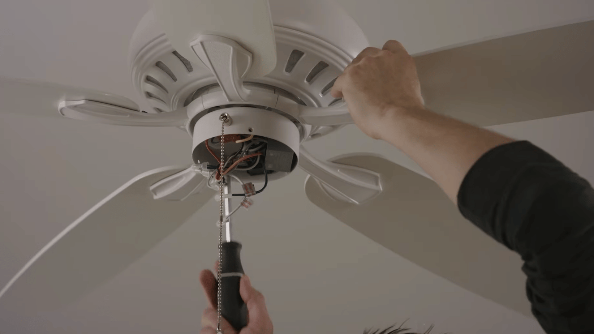 person checking ceiling fan blade arm alignment while tightening screws to correct uneven blade positioning and wobble issues