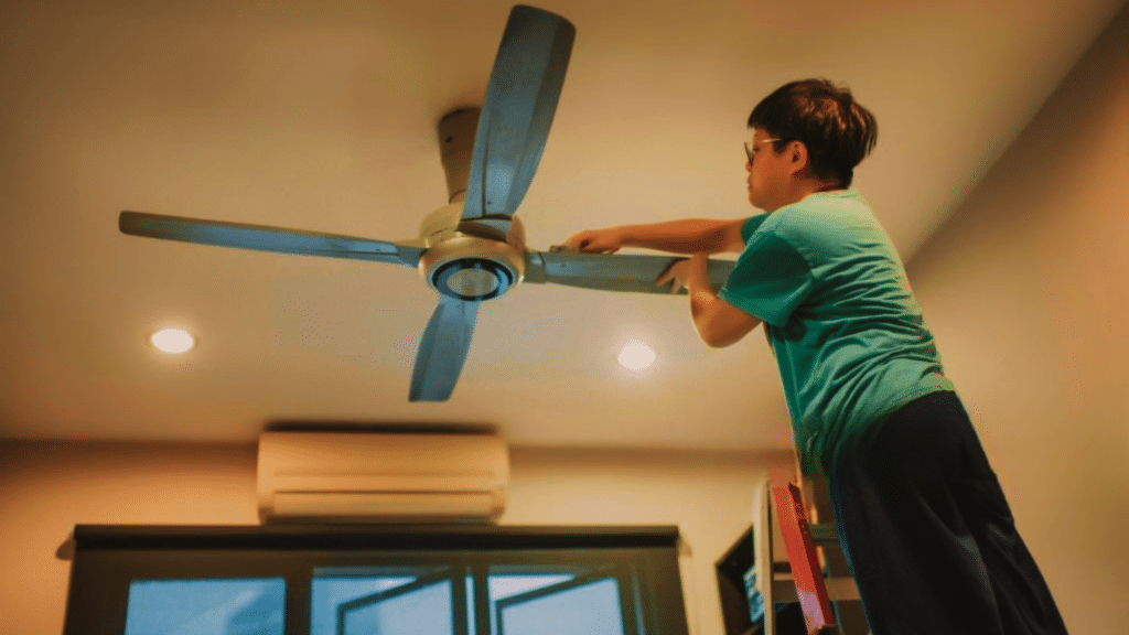 person cleaning ceiling fan blades using a step ladder and cloth at home.