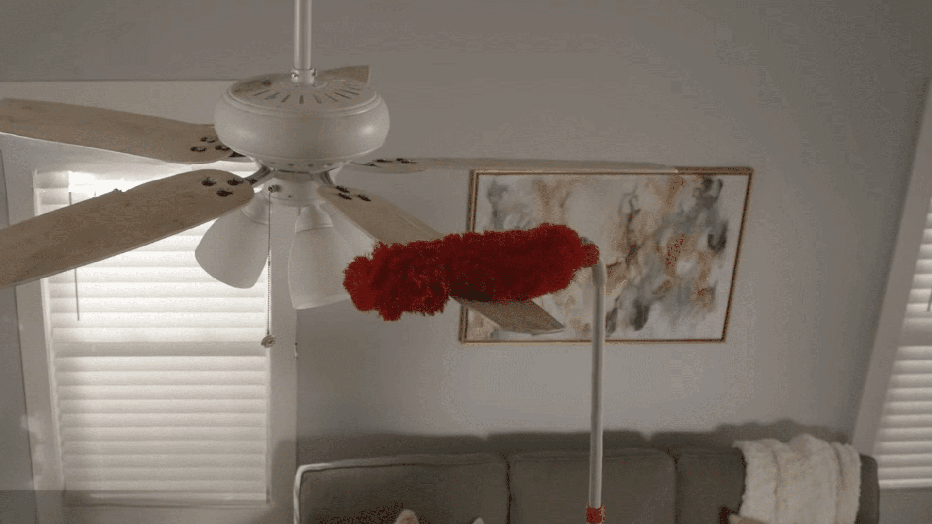 person cleaning ceiling fan blades with a duster to remove dust buildup before balancing the fan properly
