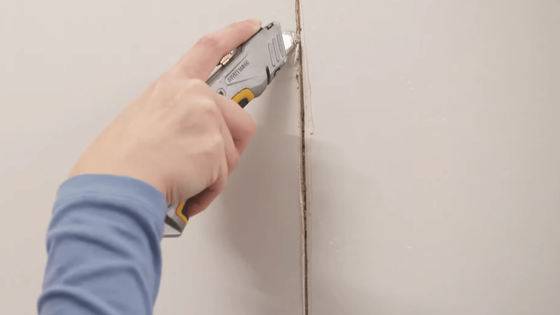 person cutting a v groove along a drywall joint with a utility knife to make taping and finishing easier later on