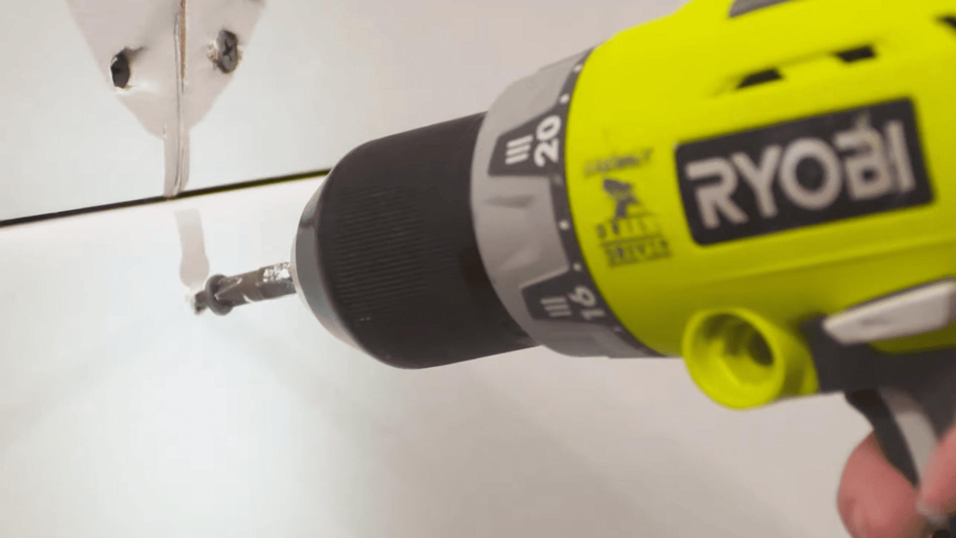 person driving a drywall screw near a corner joint to secure adjoining drywall panels during installation work
