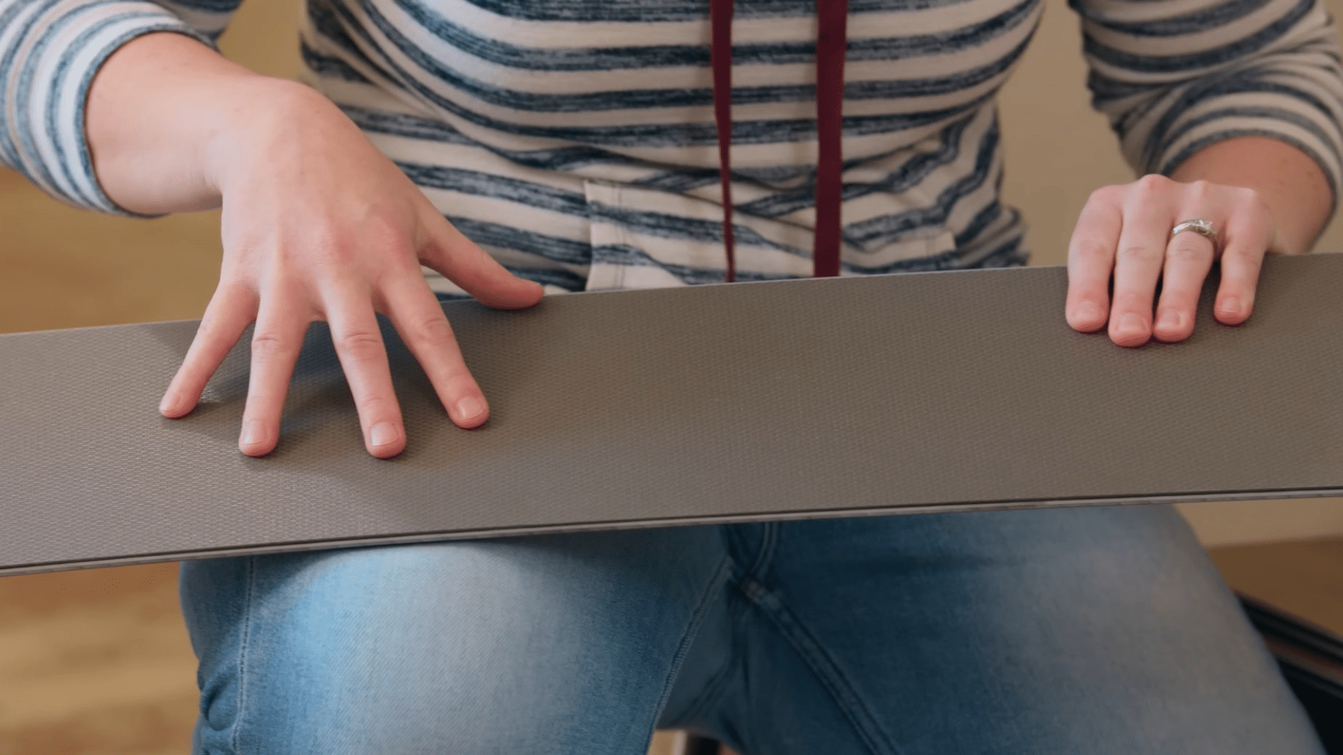 person holds a vinyl plank flooring board showing the textured backing layer before installation in a home renovation project