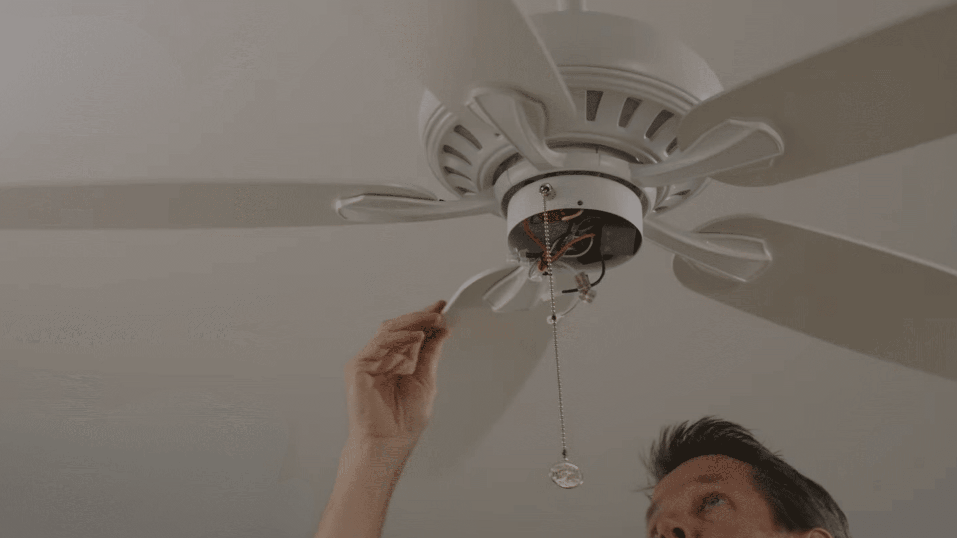 person inspecting ceiling fan blade irons for bends or damage that may cause blade misalignment and wobbling problems
