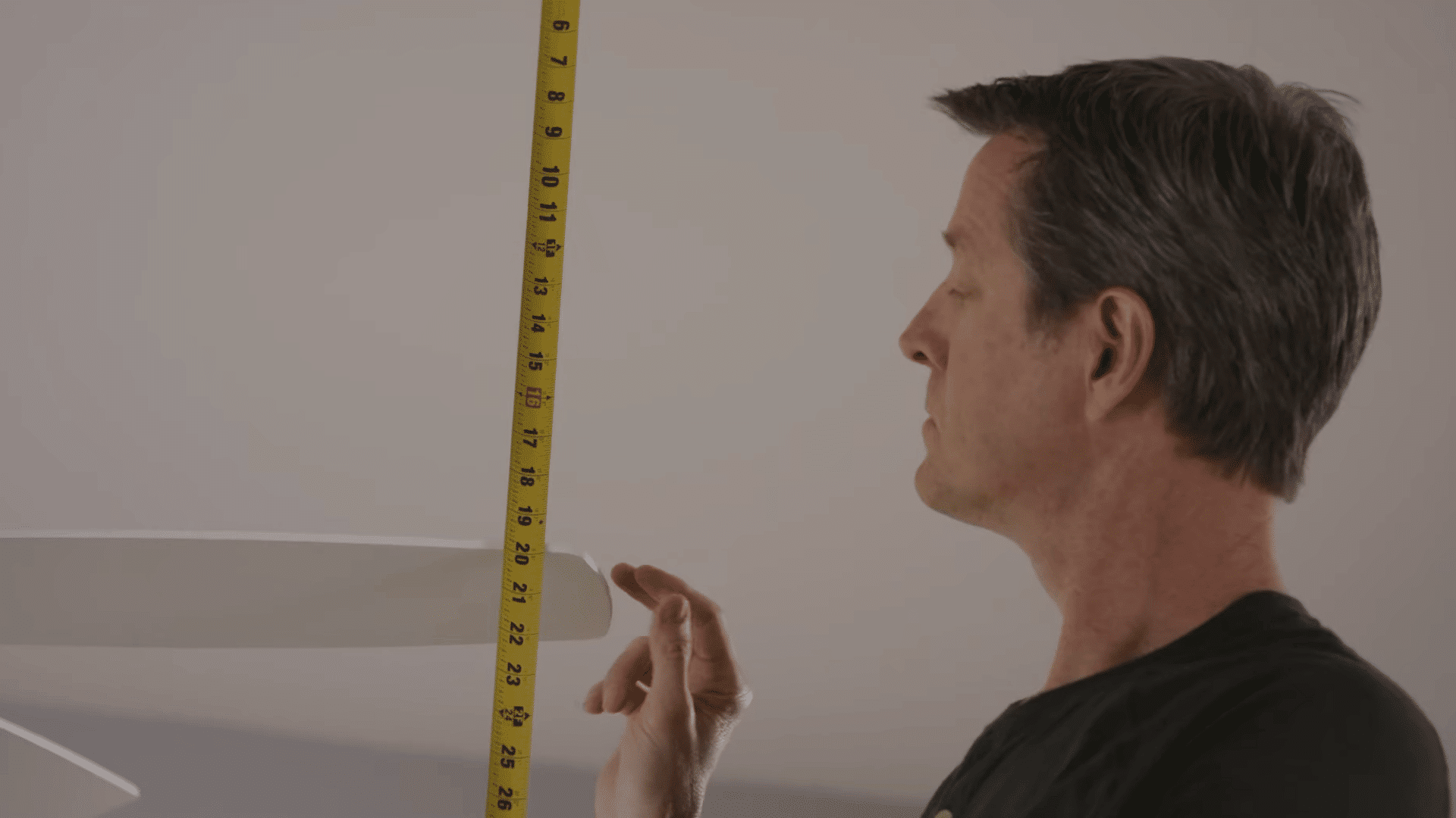 person measuring the distance between a ceiling fan blade and ceiling to check blade alignment and balance accuracy