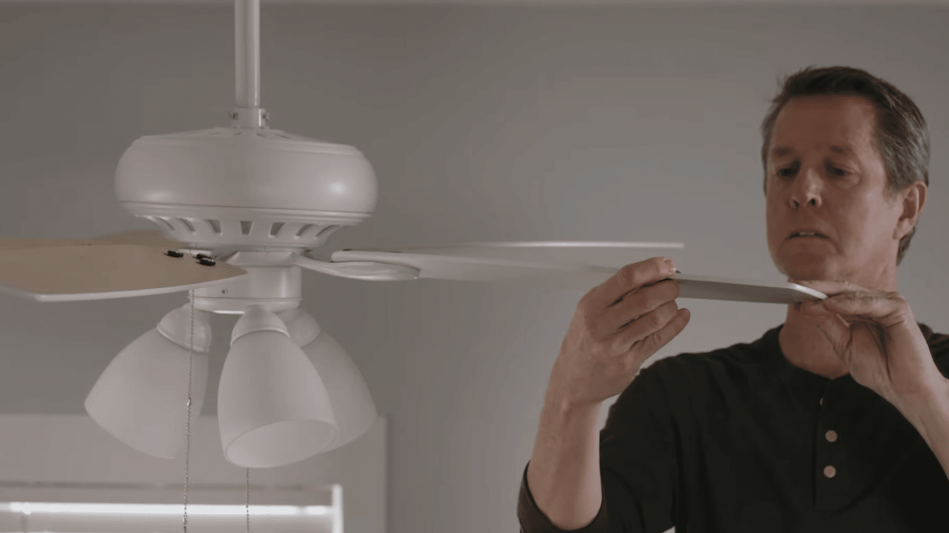 person moving a balancing clip along a ceiling fan blade to find the position that reduces wobble and improves balance