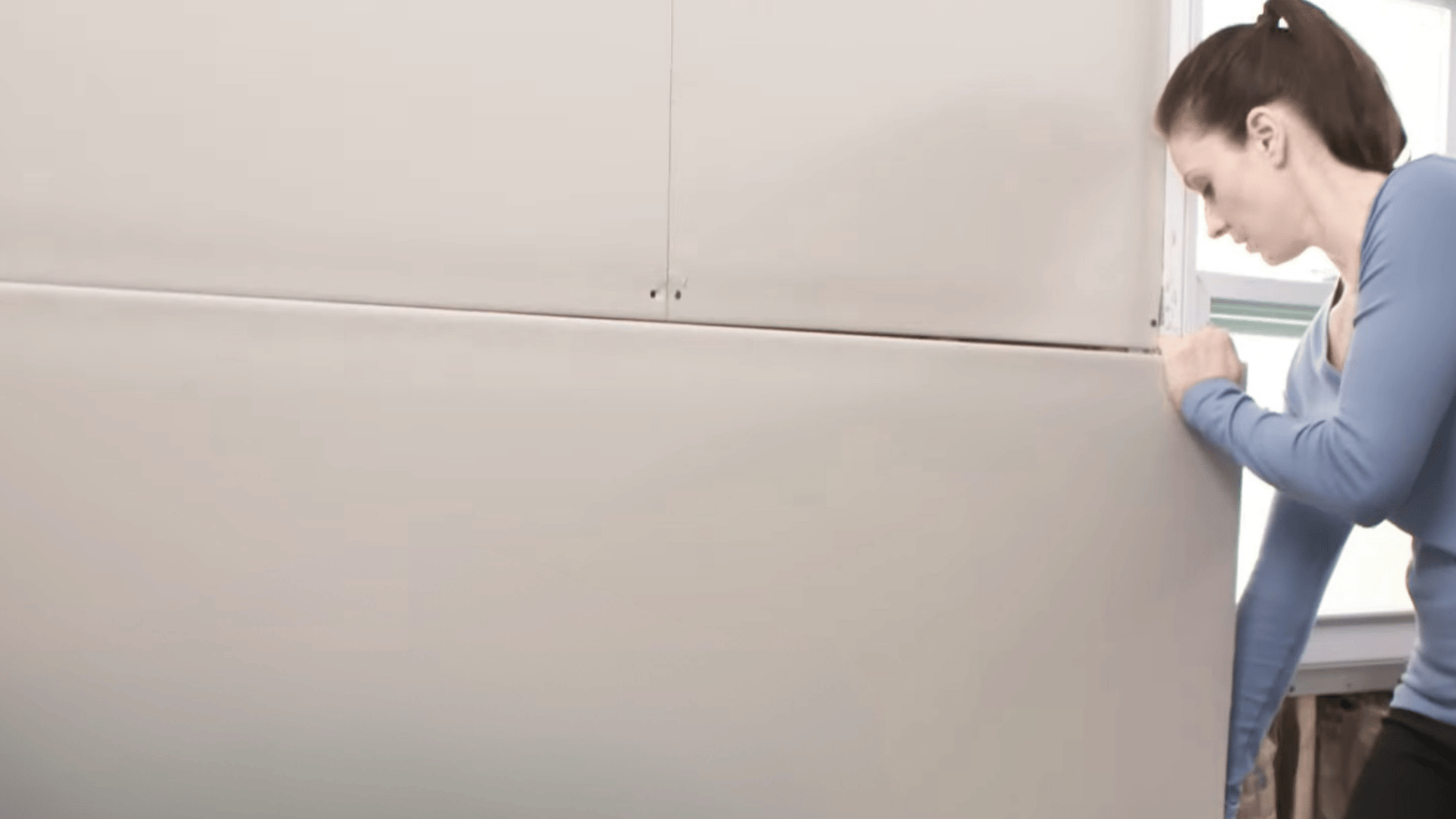person positioning a drywall sheet against a wall during installation while aligning panels for a secure fit