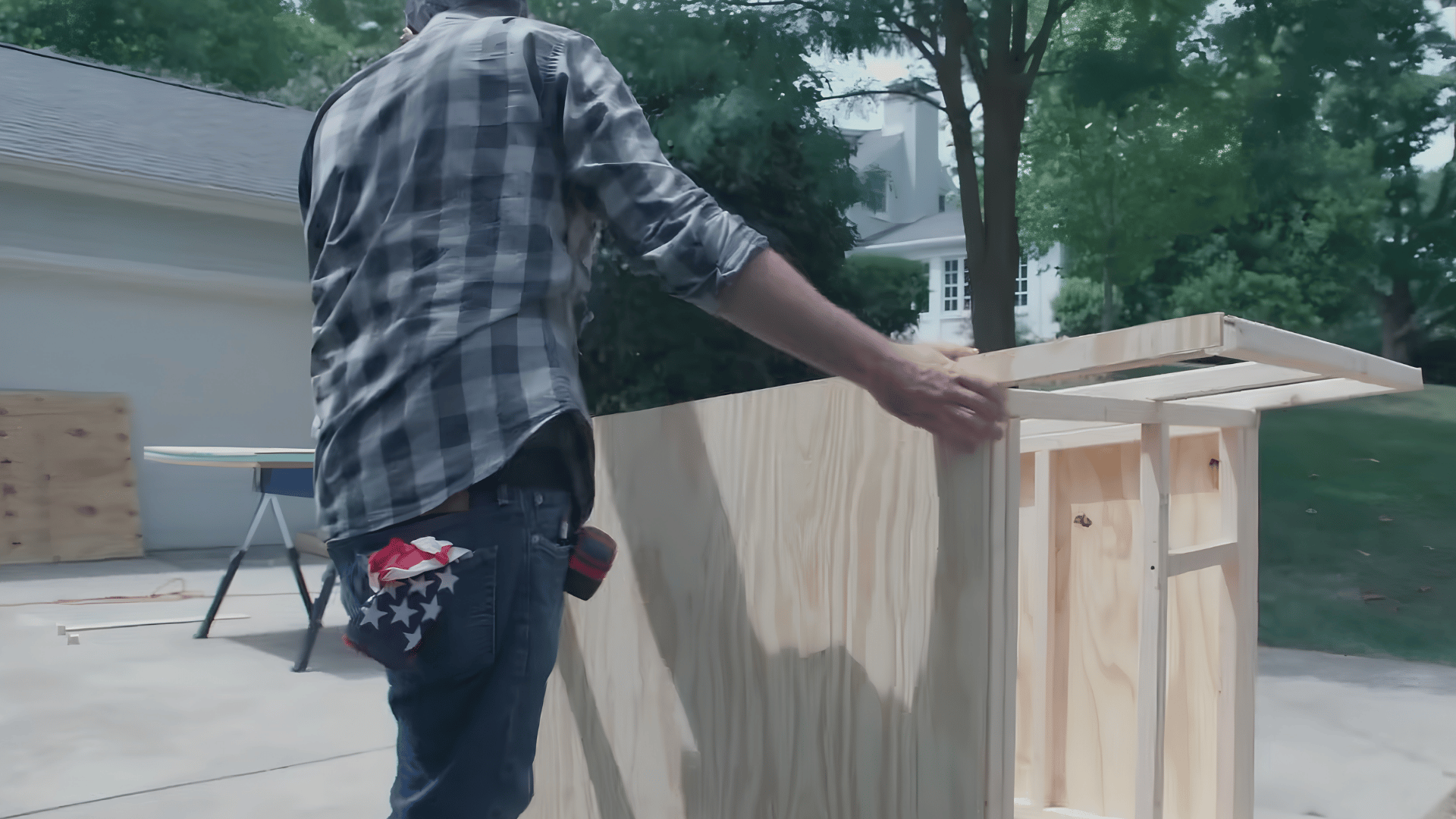 person positioning a plywood panel against a wooden framed structure while assembling an outdoor diy building project