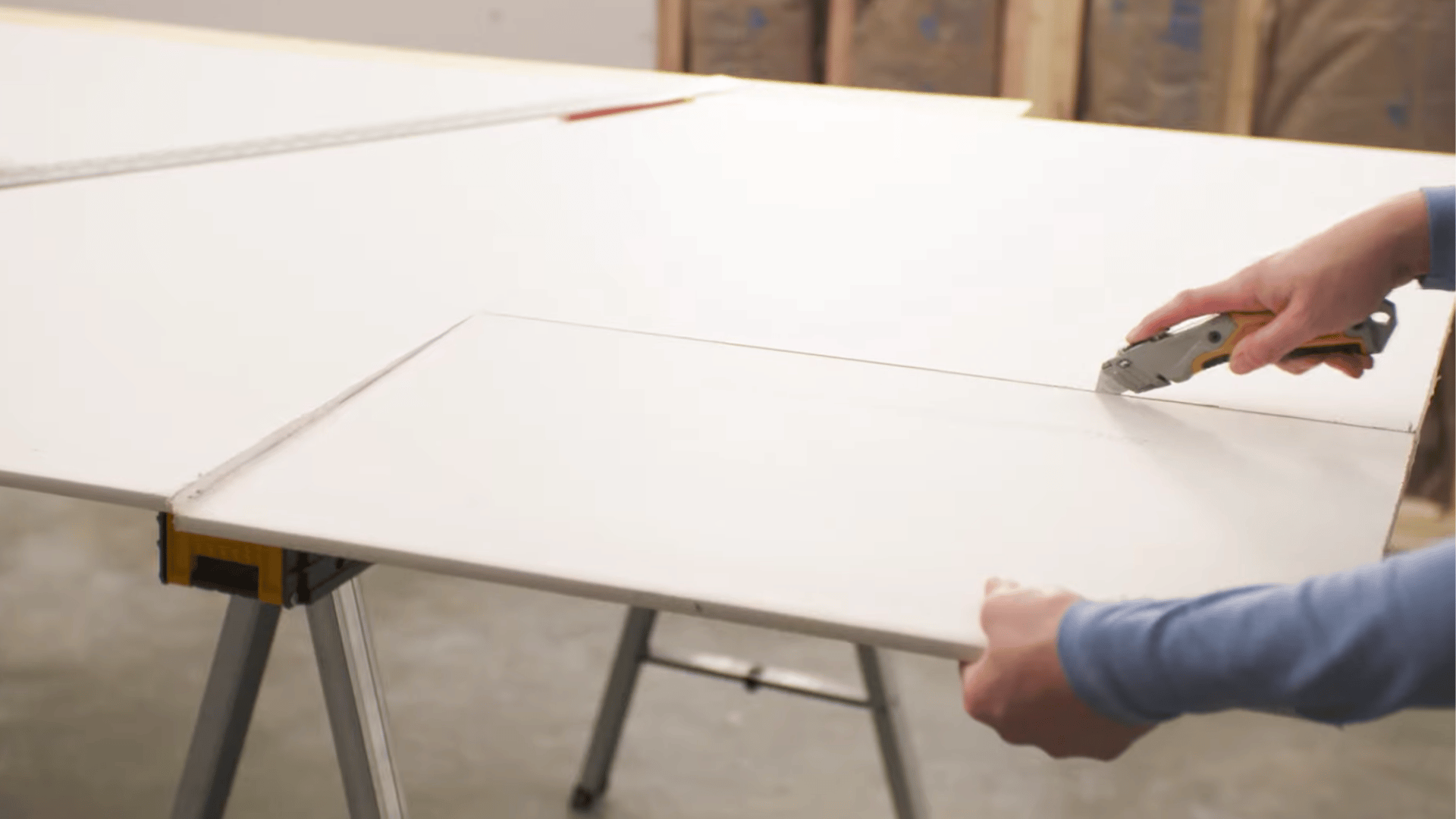 person scoring a drywall sheet with a utility knife along a marked line before making a clean cut for installation