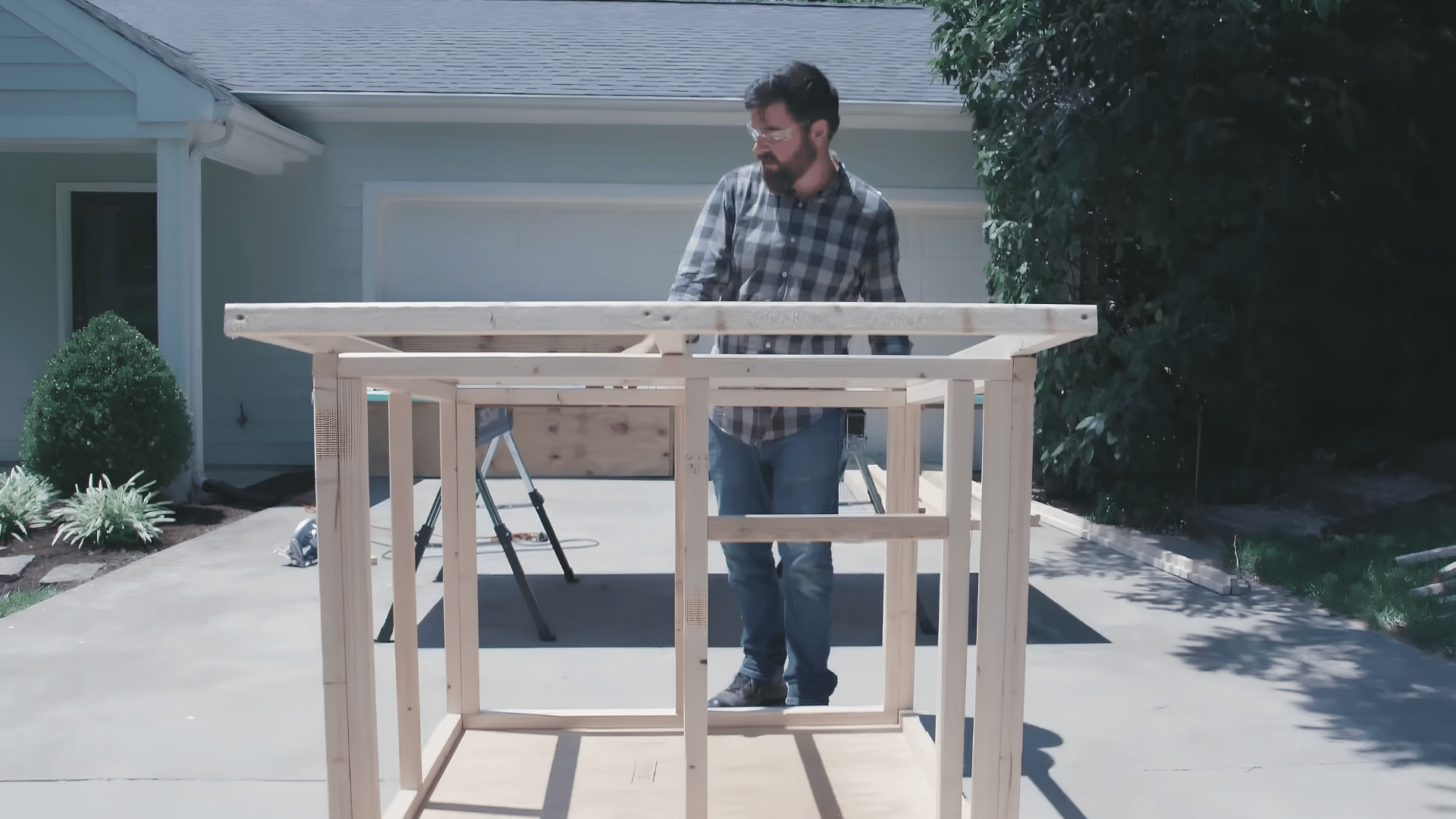 person standing behind a wooden framed structure with a roof panel attached while inspecting a diy construction project outdoors