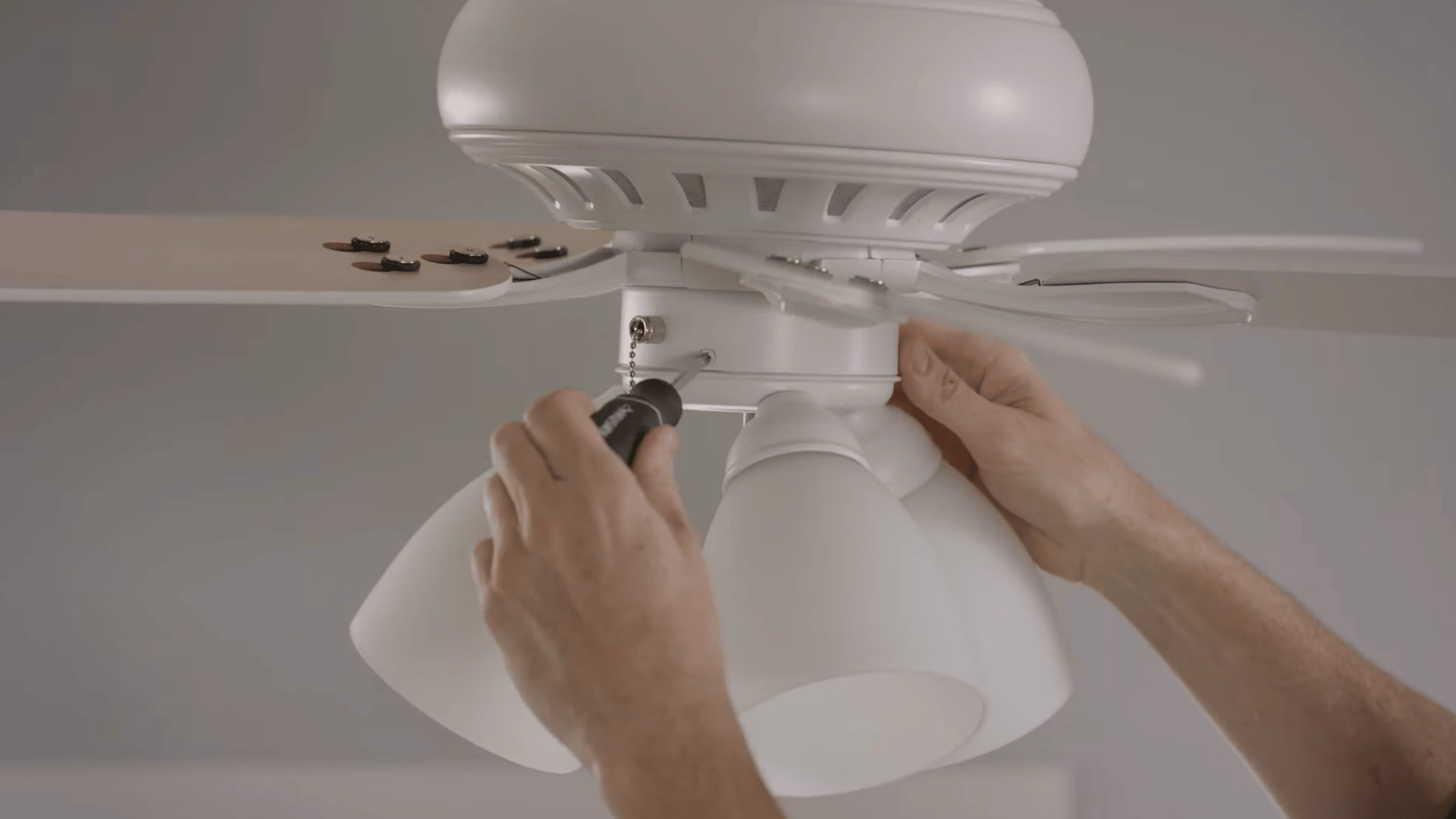 person tightening ceiling fan light kit screws to secure the housing and reduce movement that may cause wobbling