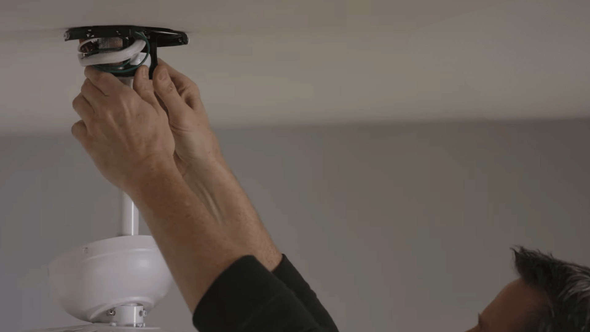 person tightening ceiling fan mounting hardware and electrical connections to secure loose fasteners and reduce wobbling