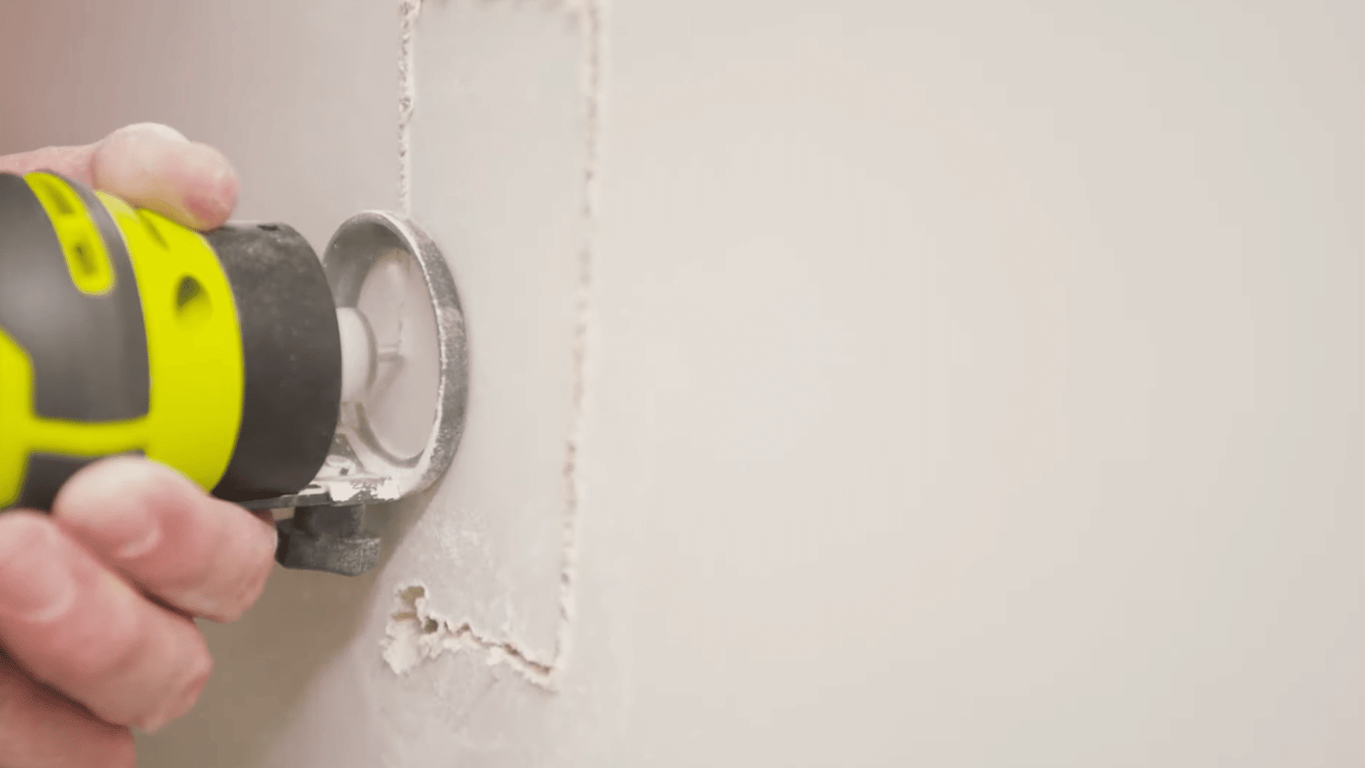 person using a drywall router to cut a clean opening in a drywall panel for an outlet or wall fixture installation