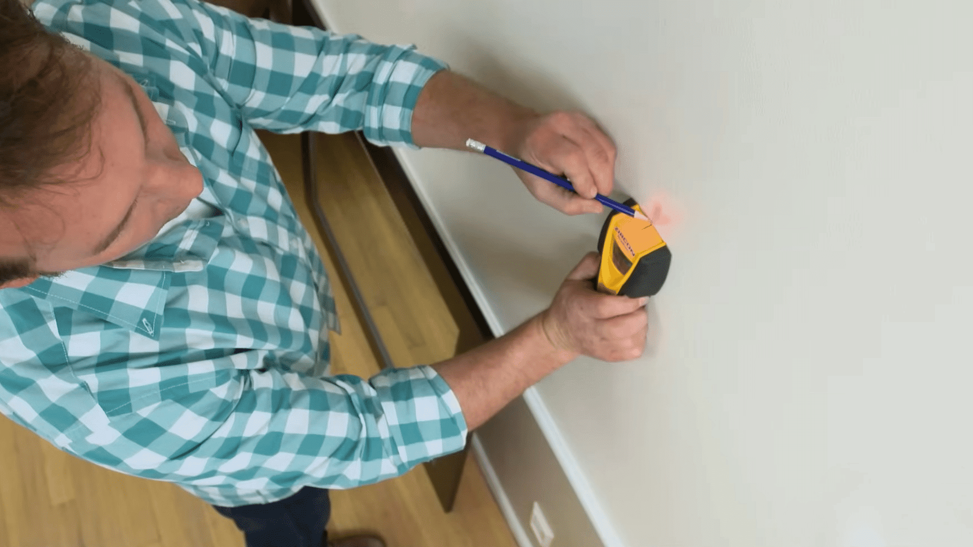 person using a stud finder and pencil to mark a wall location before installing hardware to hang a framed picture