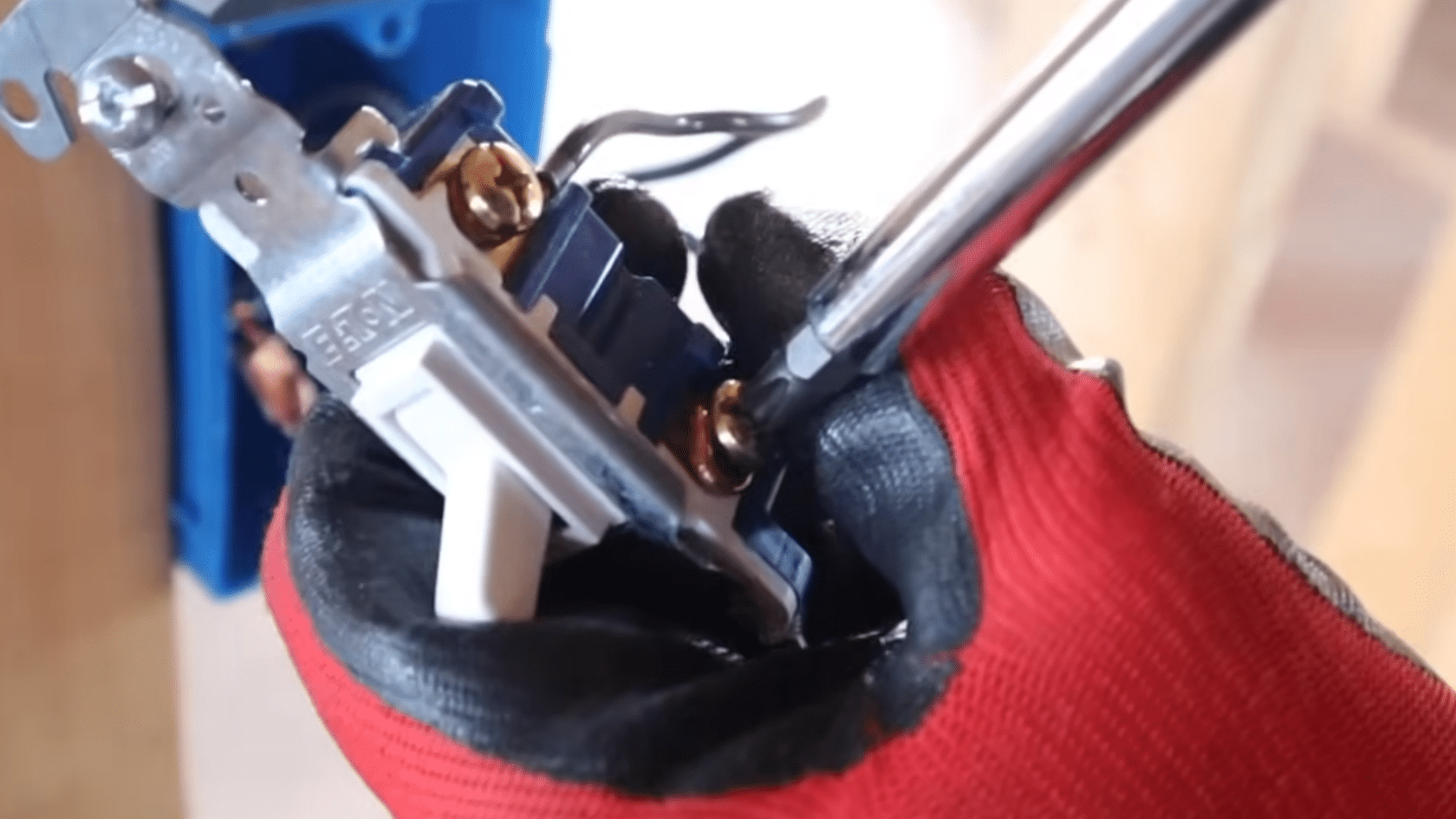 person wearing red and black work gloves uses a screwdriver to secure a wall switch during electrical installation