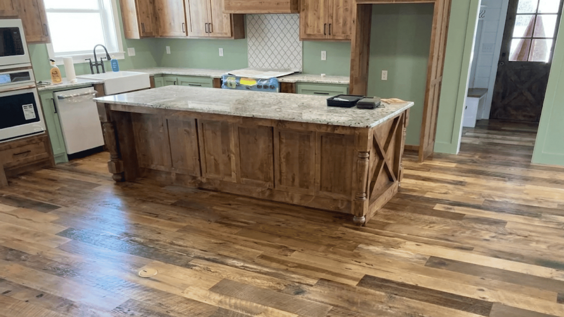 rustic kitchen with wood cabinets large island farmhouse sink and mixed tone hardwood flooring throughout the space