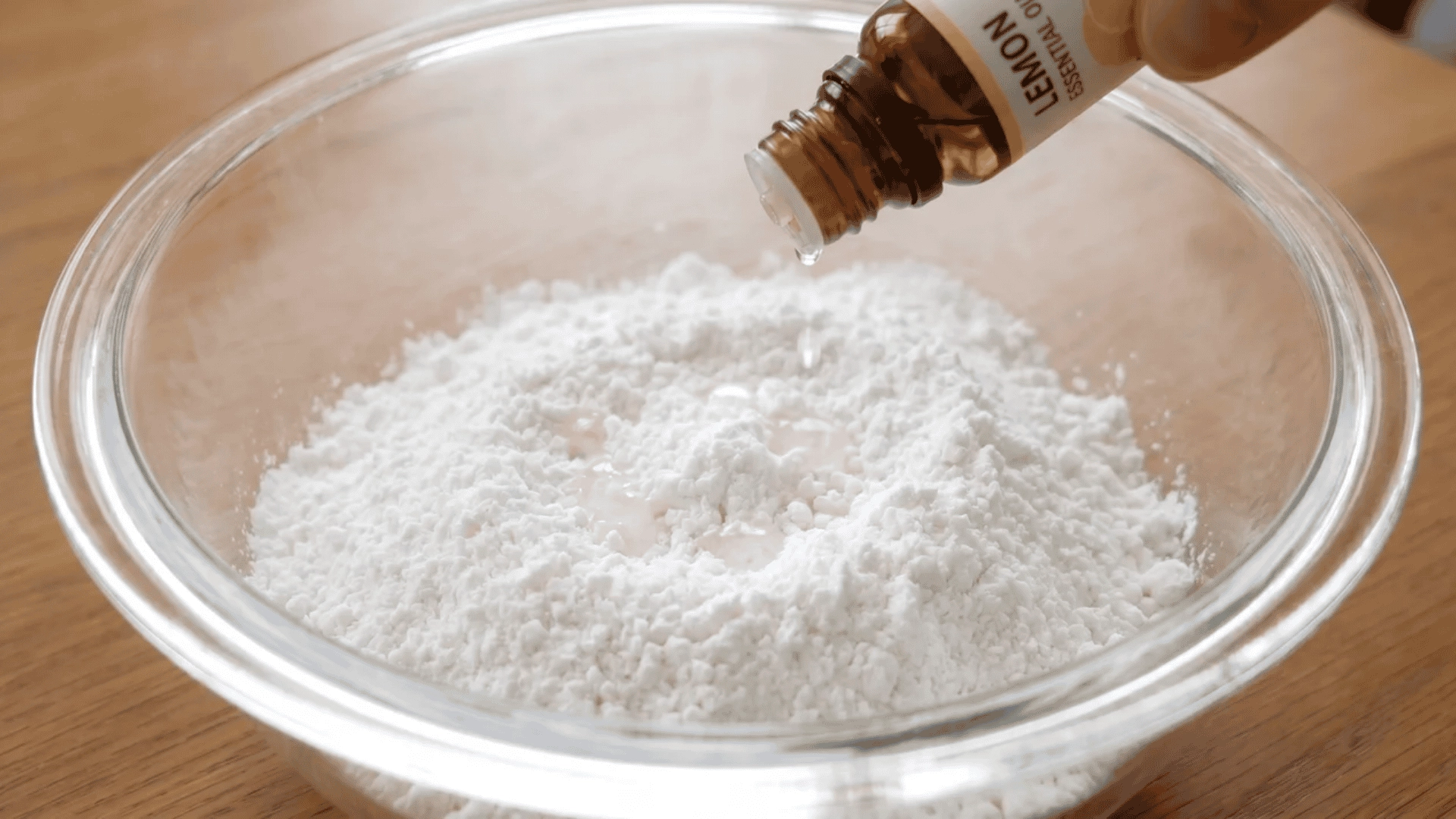 A few drops of lemon essential oil being added to DIY dishwasher detergent powder in a bowl for a fresh scented finish.