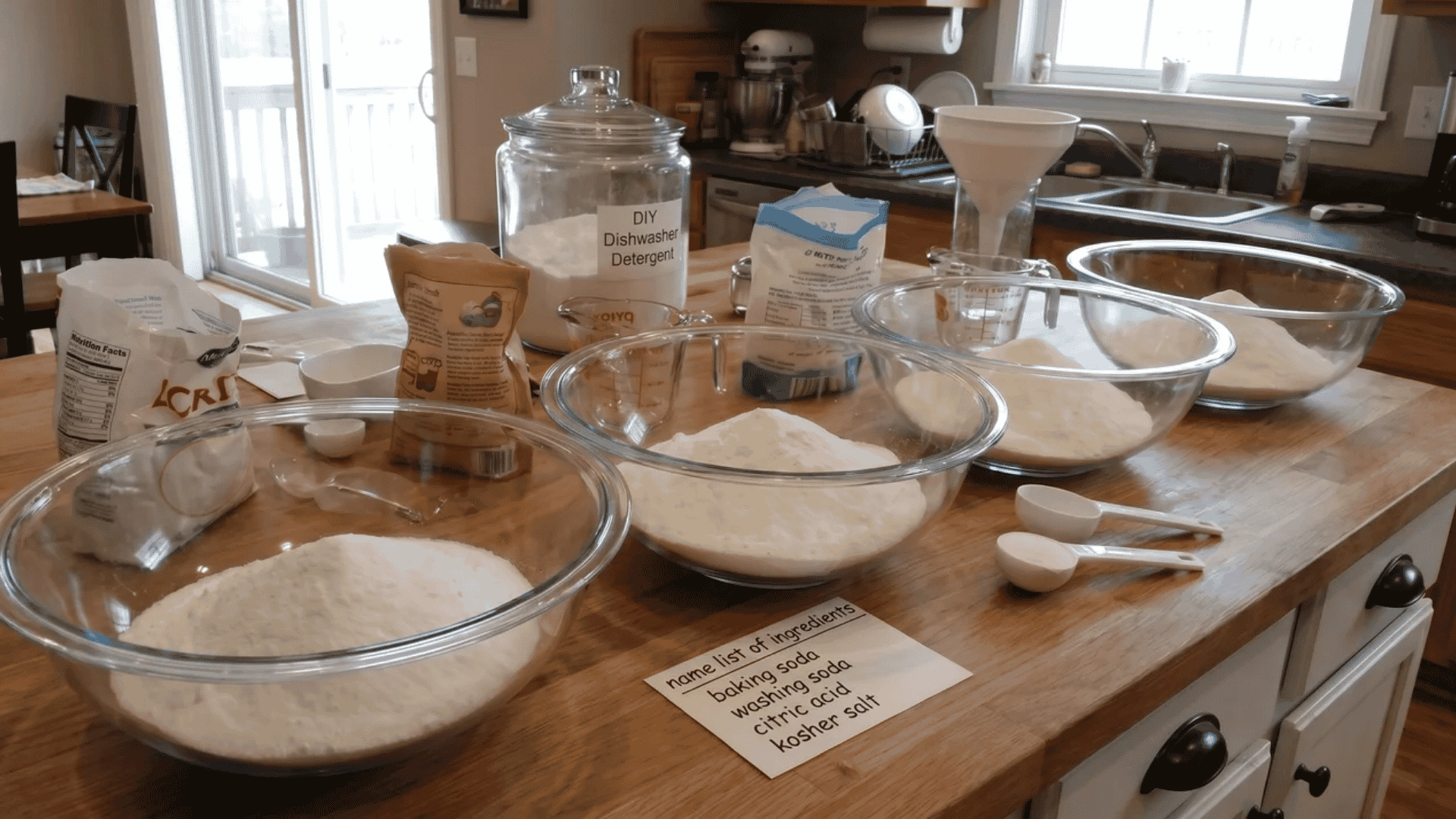 Several large bowls on a counter filled with measured powders, illustrating how to scale up the DIY dishwasher detergent recipe.