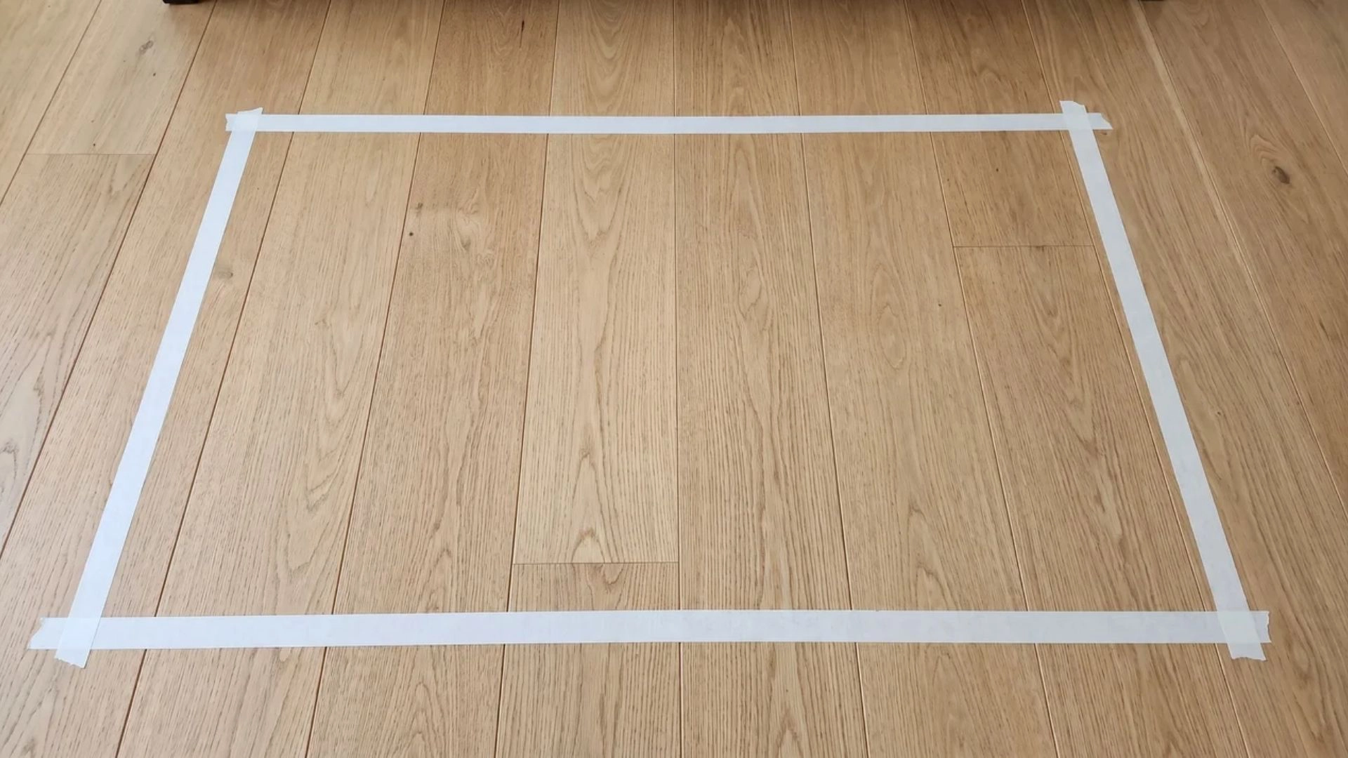 Painter’s tape outlining furniture footprint on floor, showing room spacing and proportion before buying.