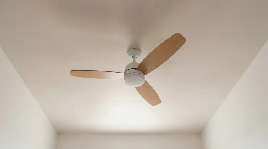 Ceiling fan centered on bedroom ceiling in a simply furnished room with neutral walls